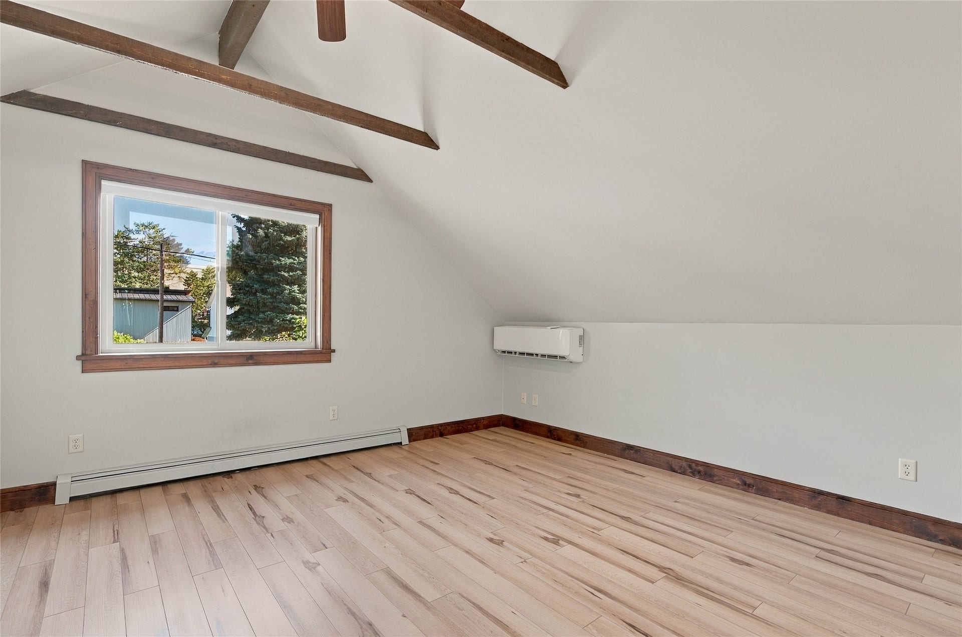 Vaulted ceiling with exposed wood beams, light wood-finish flooring, and a mini-split system