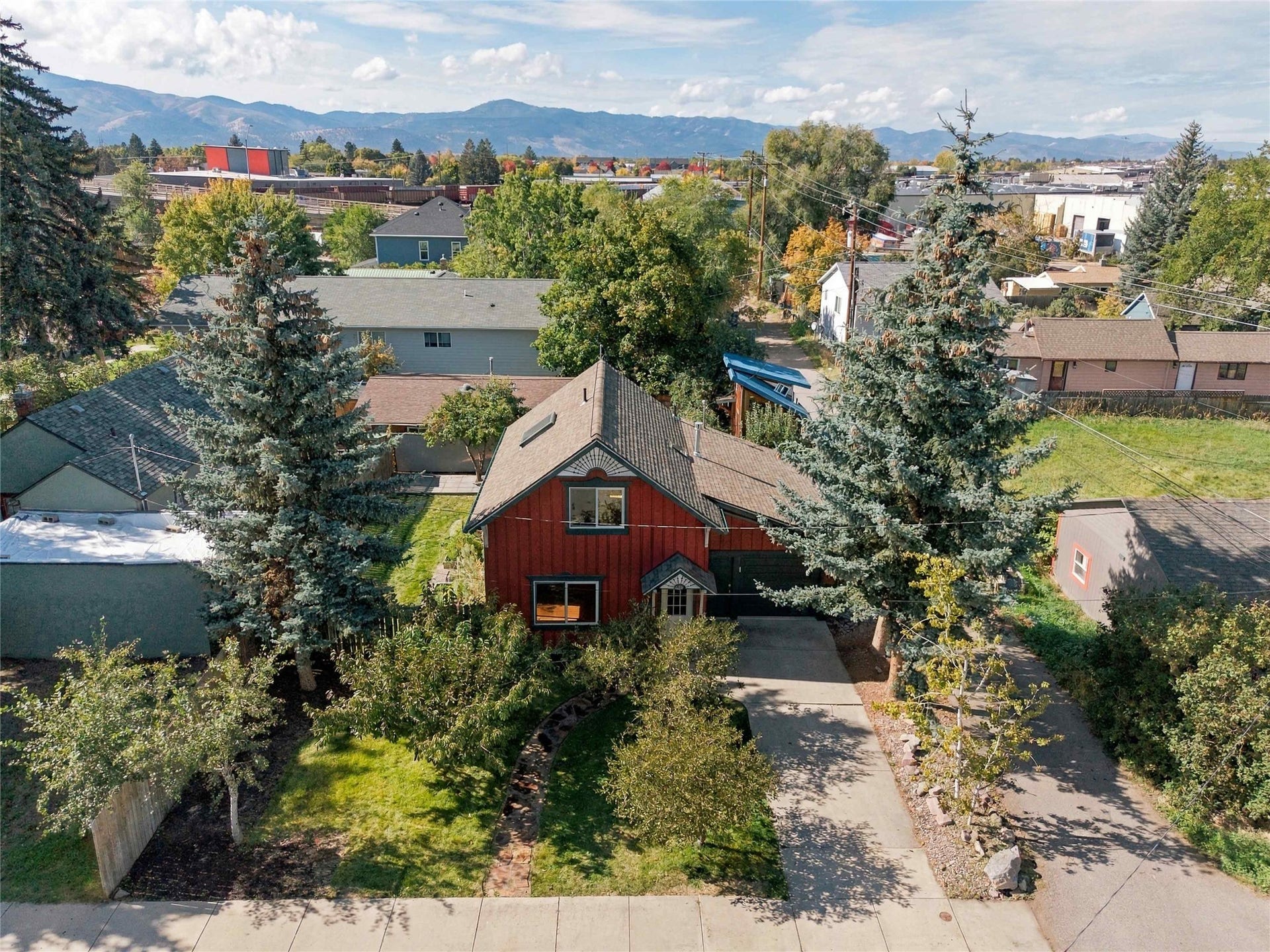 Red siding exterior with a pitched roof, front entry with covered porch, concrete driveway, and mature landscaping