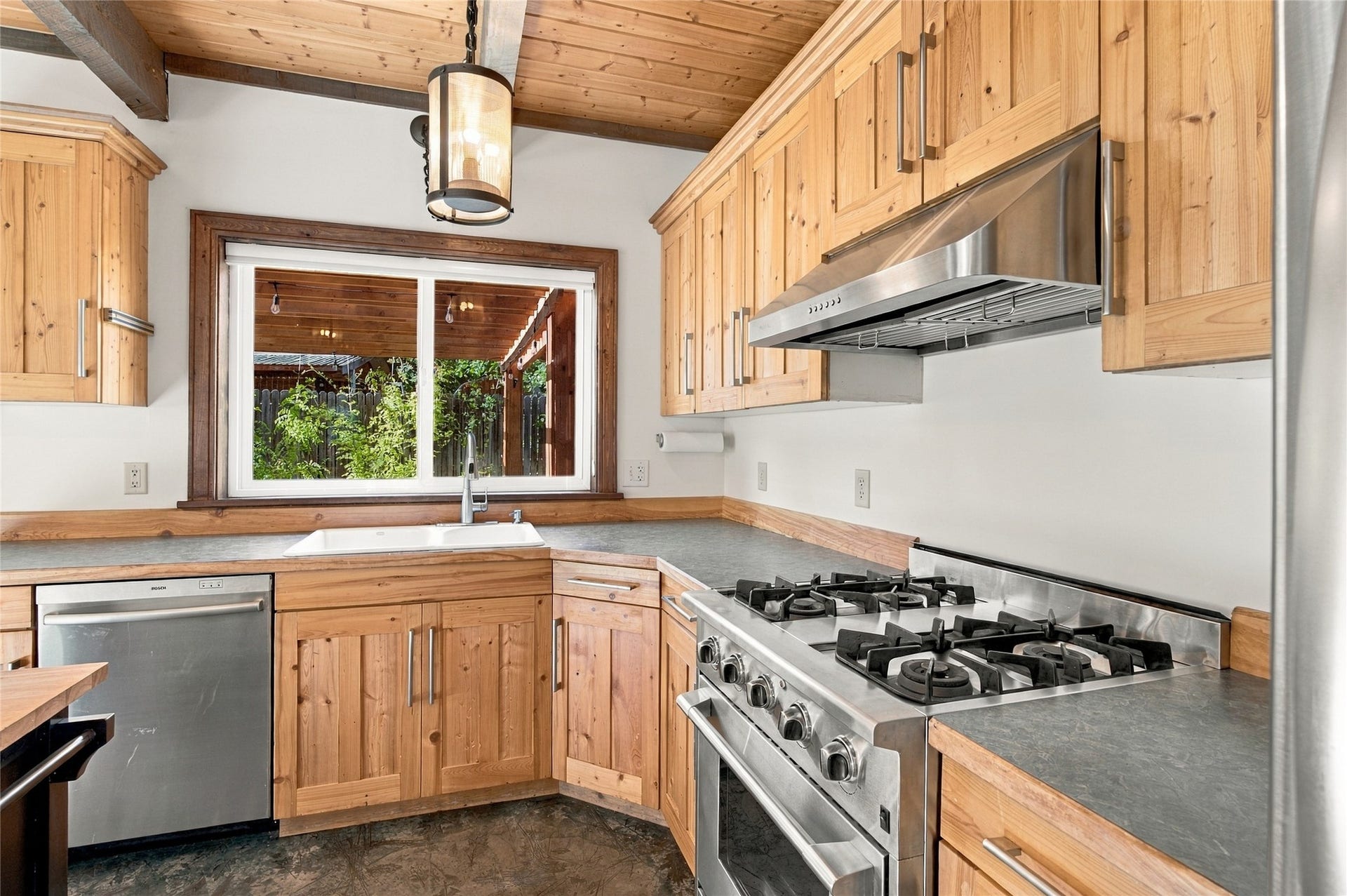 Kitchen featuring wood cabinetry, stainless steel appliances, a window with a sink, and a wood-paneled ceiling with exposed beams