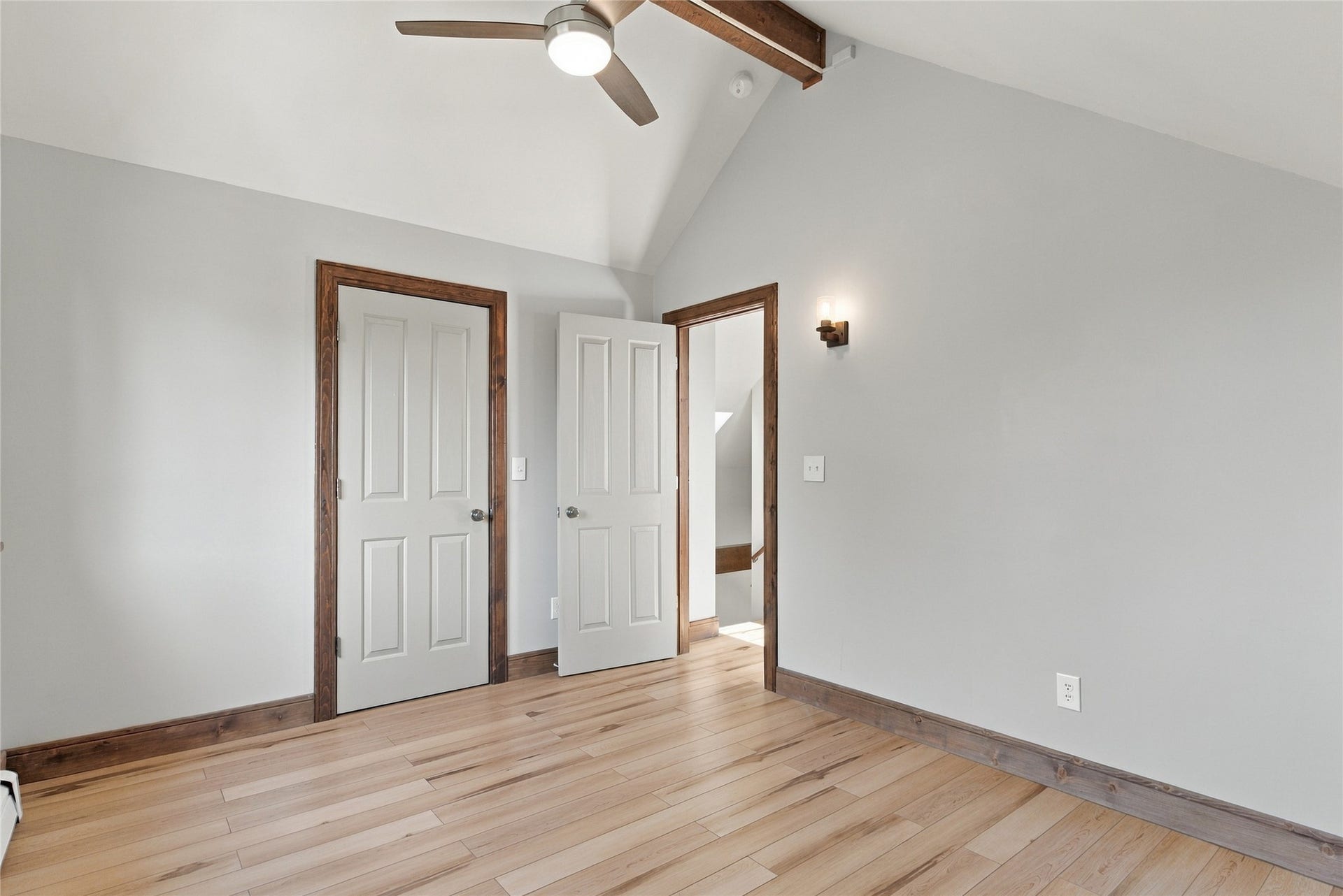 Vaulted ceiling featuring a wood-finish beam, light wood-finish flooring, two panel doors, and a ceiling fan with integrated lighting