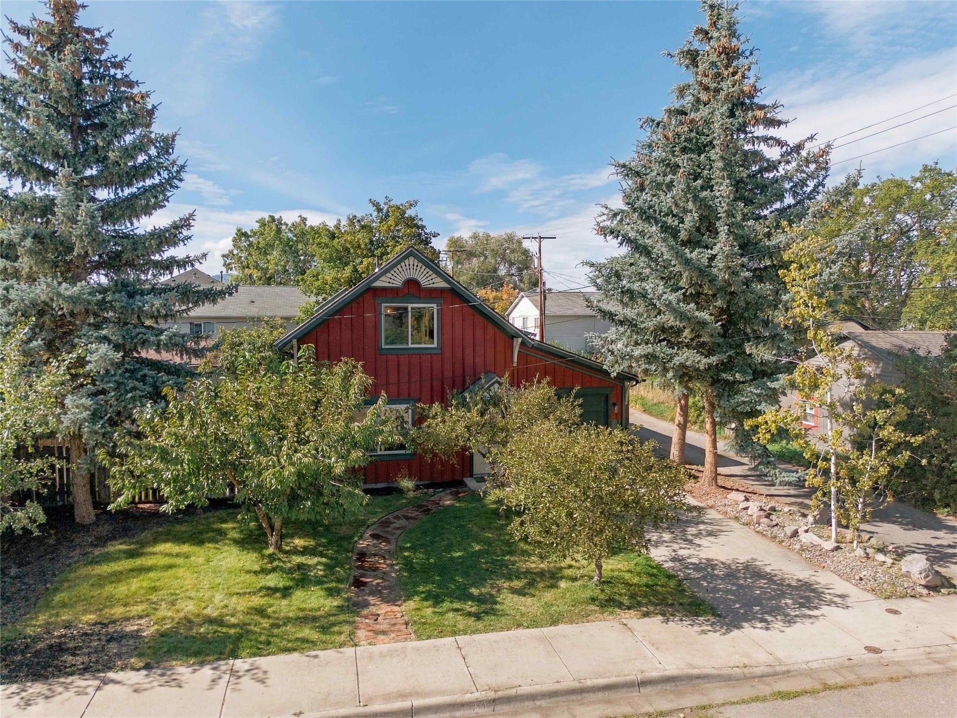 Red exterior siding with white trim, arched window detail, established lawn, concrete driveway, and mature trees