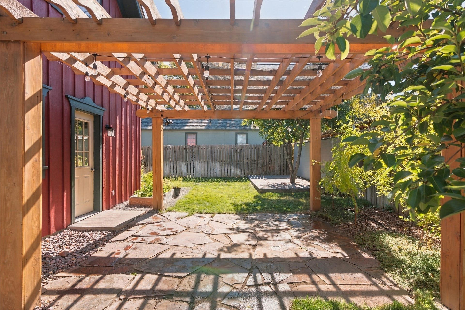 Expansive flagstone patio with a wooden pergola structure, string lighting, and a manicured lawn