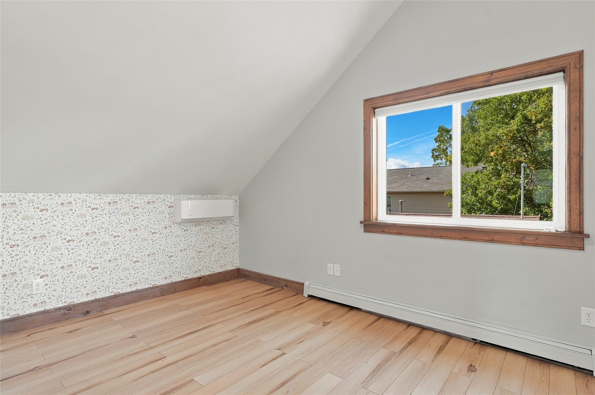 Wood-finish flooring, accent wall with patterned wallpaper, mini-split unit, and a window with wood trim