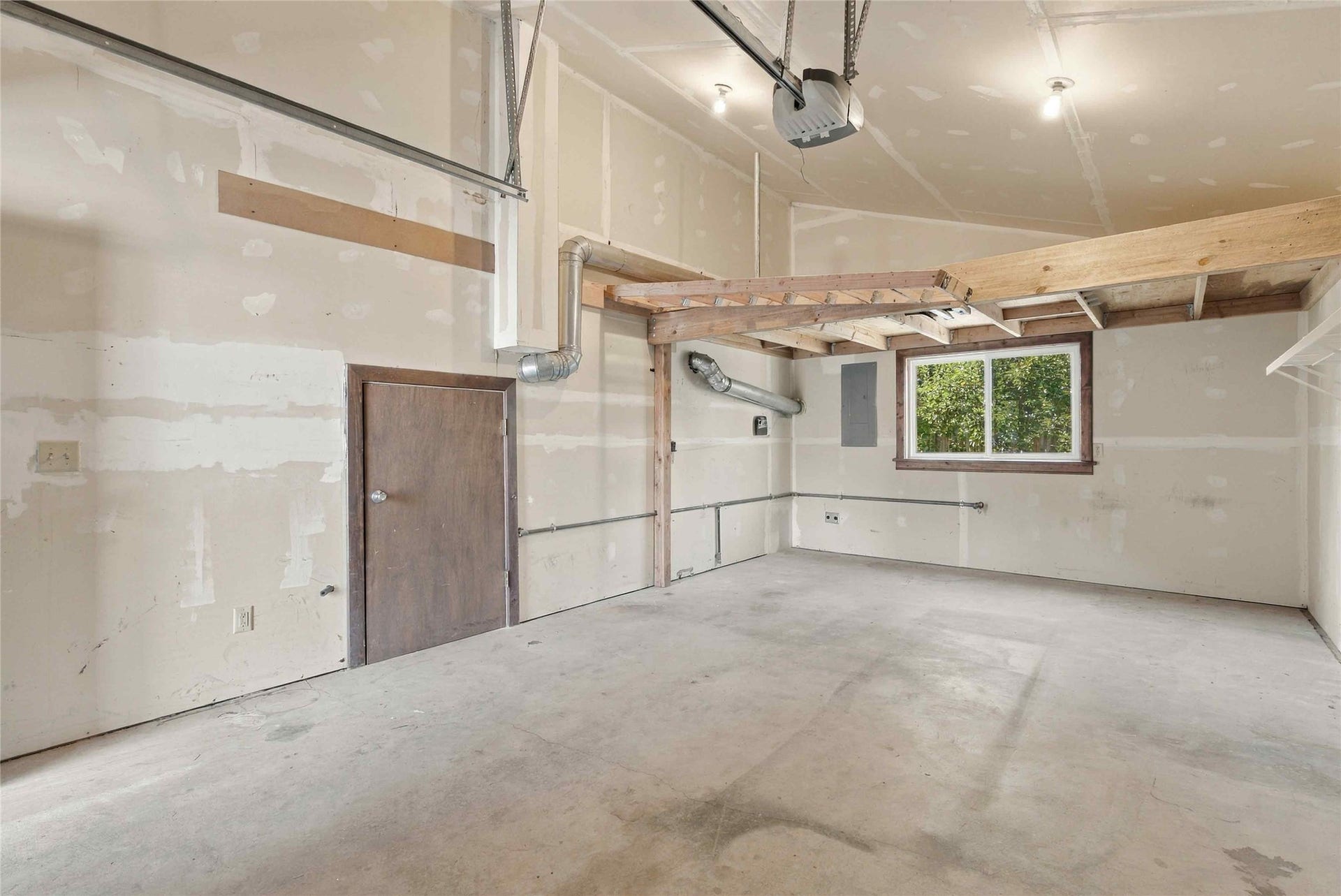 Concrete flooring, drywall walls, overhead garage door mechanism, single window, and exposed wood framing