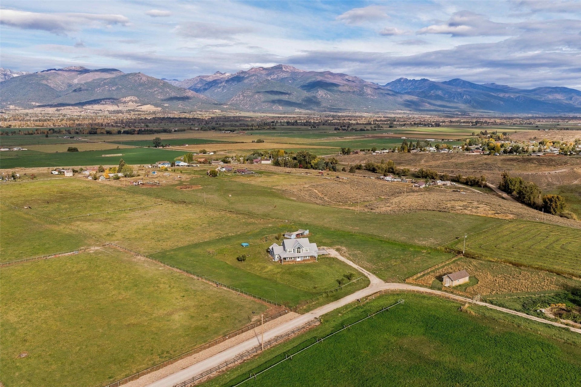 Expansive property featuring a residence with a light-toned roof, multiple outbuildings, a gravel drive, and a backdrop of distant mountains