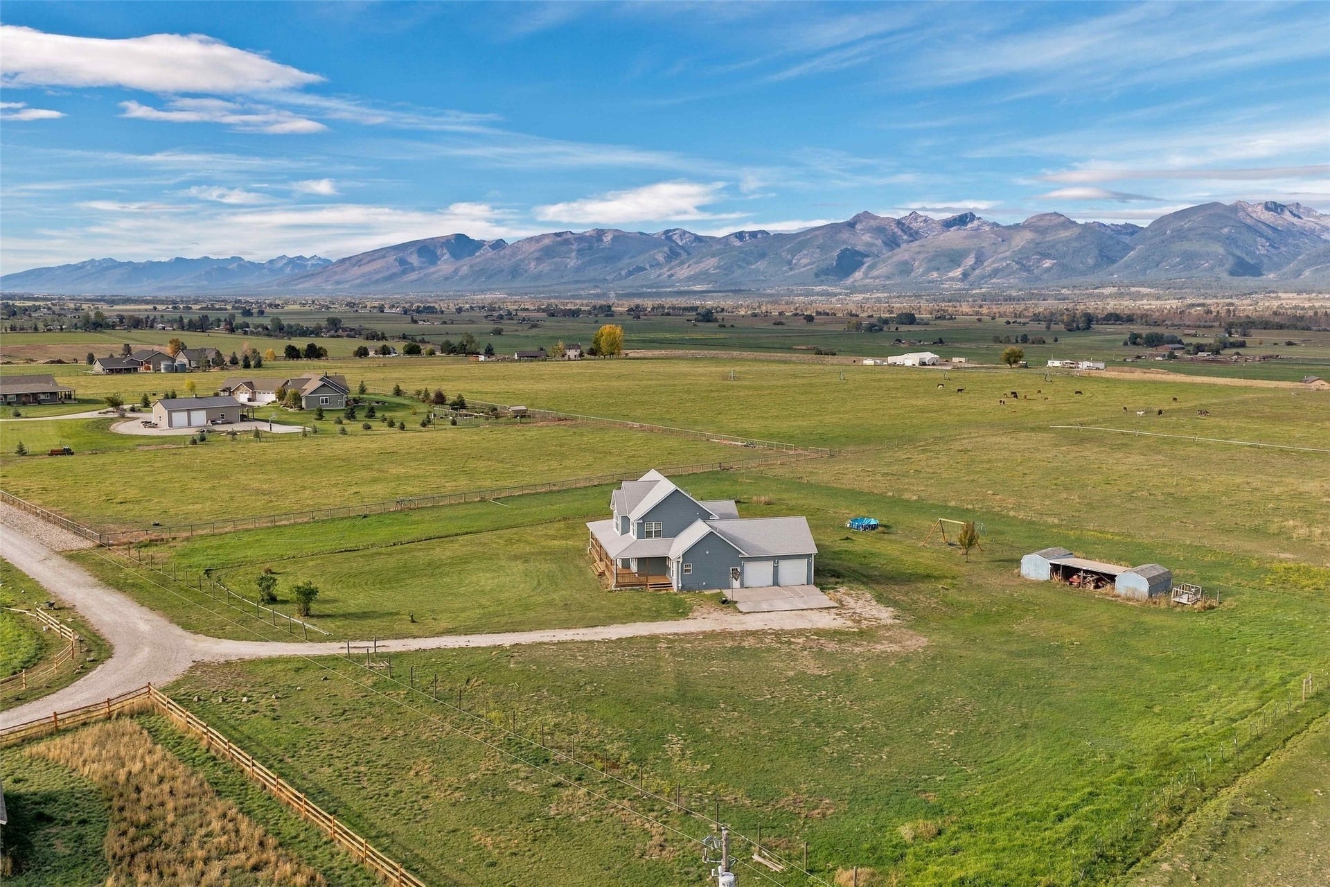 Expansive green acreage with distant mountain ranges, featuring a two-story residence with a covered porch, an attached two-car garage, and an additional outbuilding