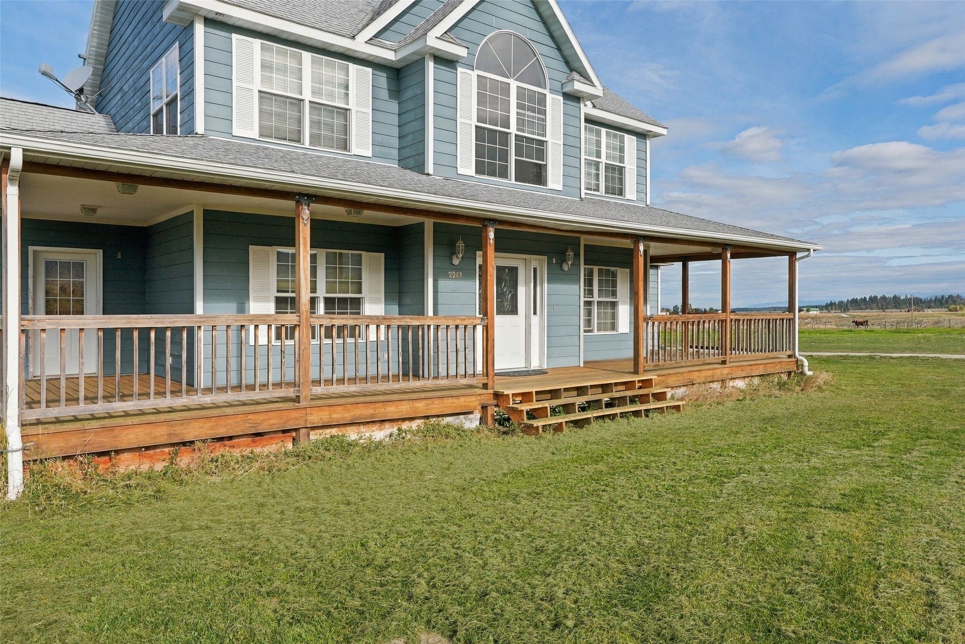 Two-story residence featuring blue siding, white window shutters, and a covered wraparound porch with wood railings and posts