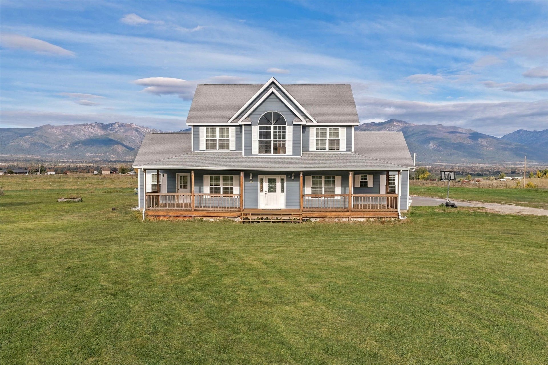 Expansive green lawn surrounding a two-story home with a wrap-around porch and arched window