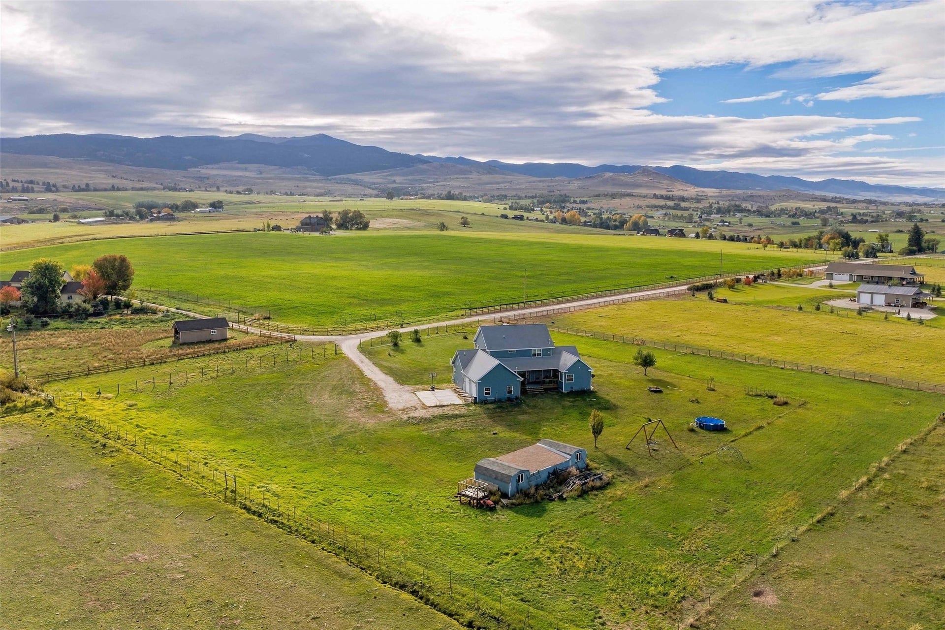 Expansive green fields, mountains, and a two-story residence with a porch