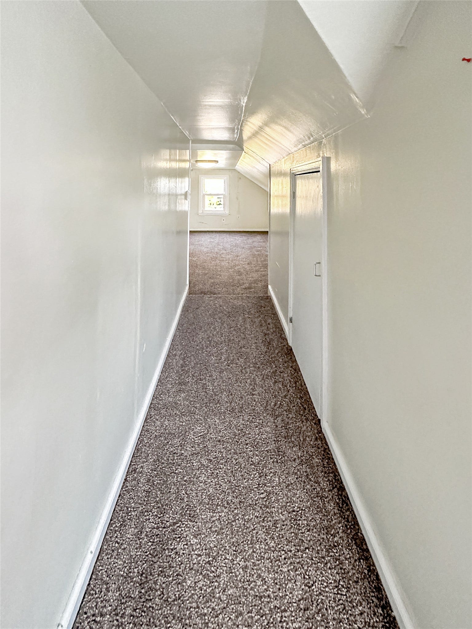 1123 2nd Street N, Shelby, MT 59474 Hallway with textured carpeting, white painted walls, and a white painted ceiling, leading to a room with a window
