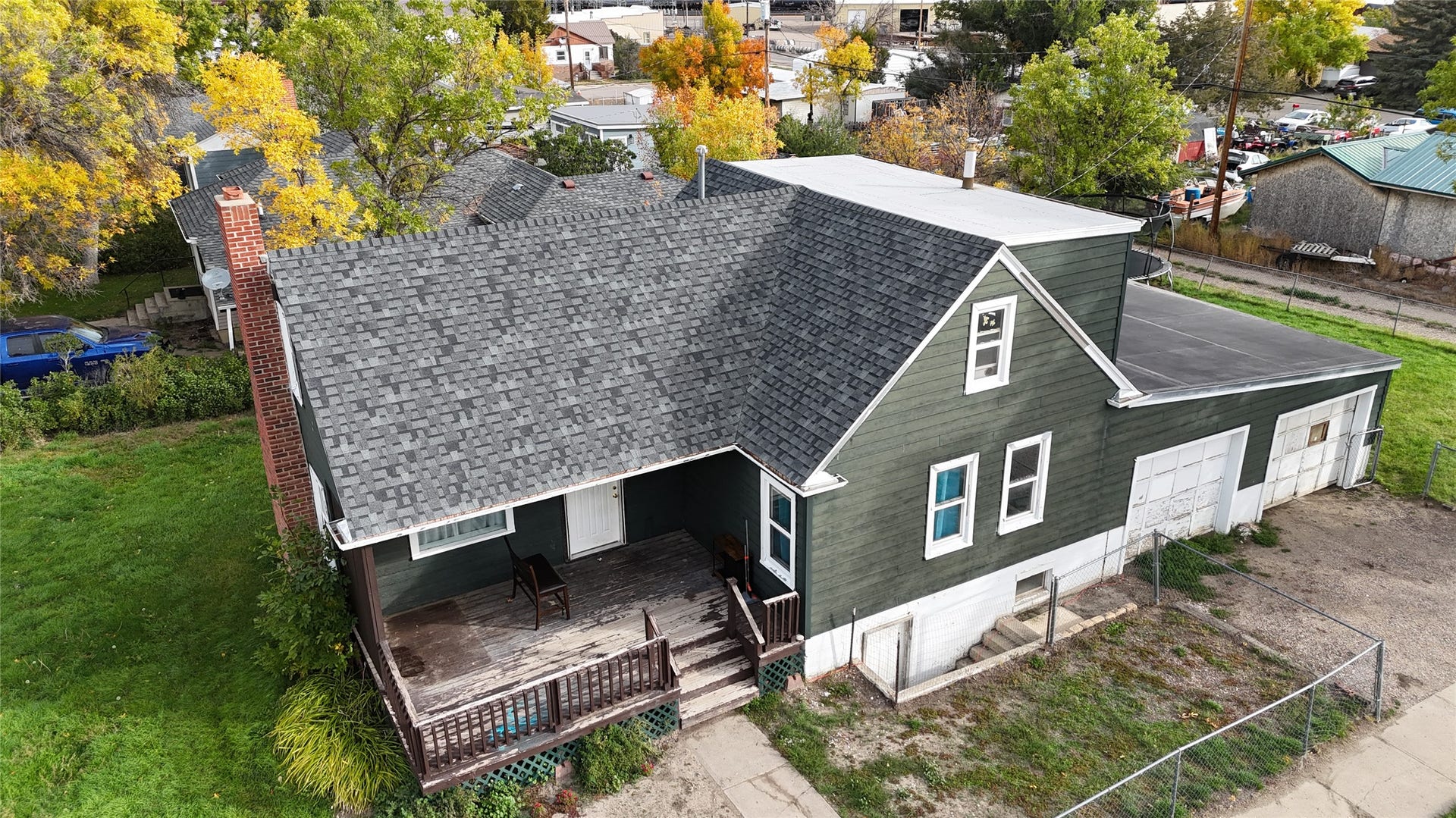 1123 2nd Street N, Shelby, MT 59474 Exterior featuring dark green siding, a shingled roof, a brick chimney, and an attached two-car garage