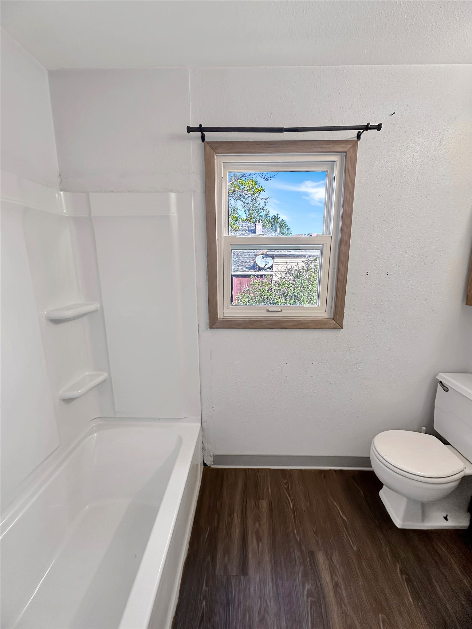 1123 2nd Street N, Shelby, MT 59474 White bathtub and shower surround with built-in shelving, wood-finish flooring, and a window with wood trim