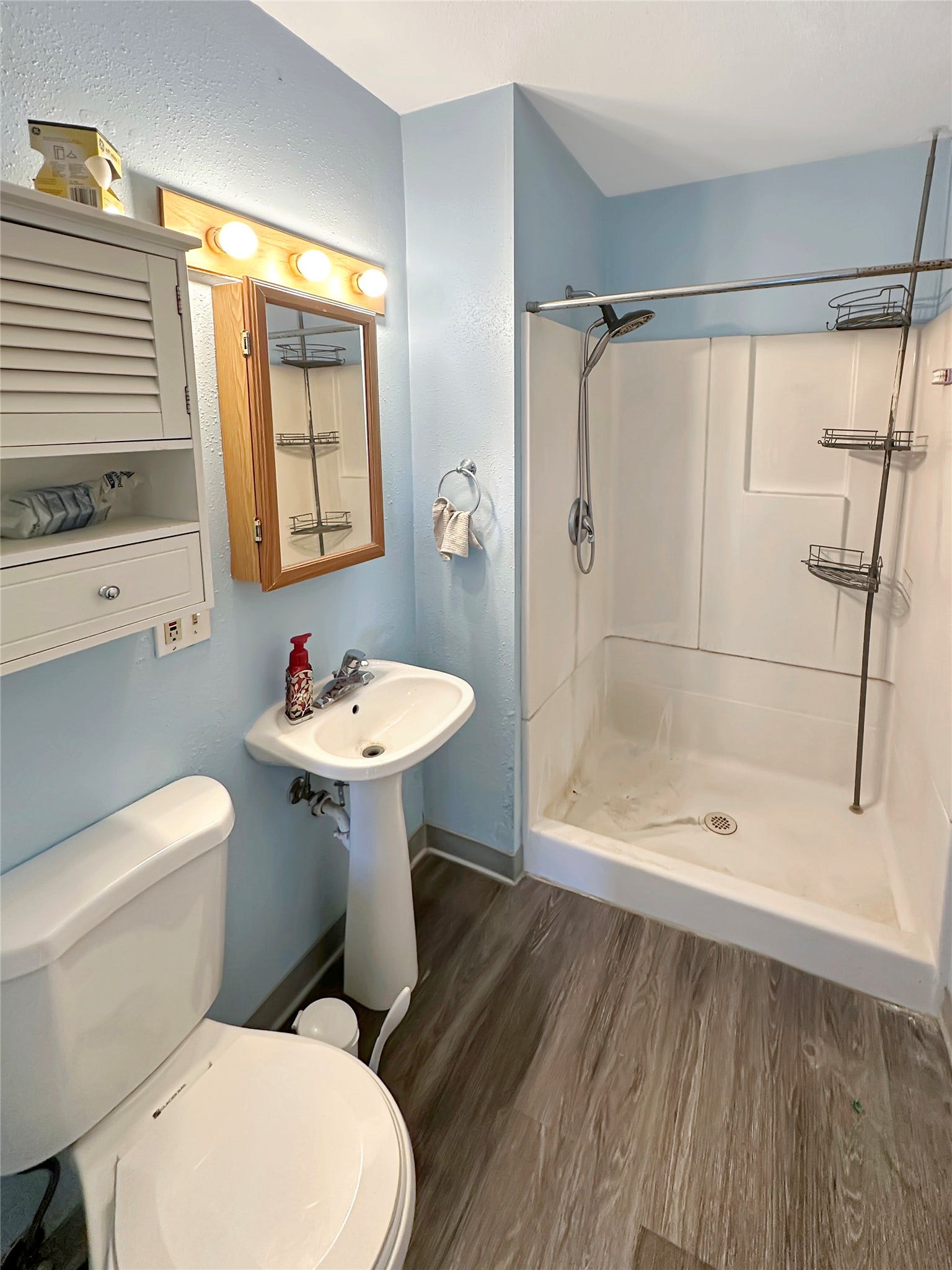 1123 2nd Street N, Shelby, MT 59474 Pedestal sink with chrome faucet, light wood-finish flooring, and white shower enclosure
