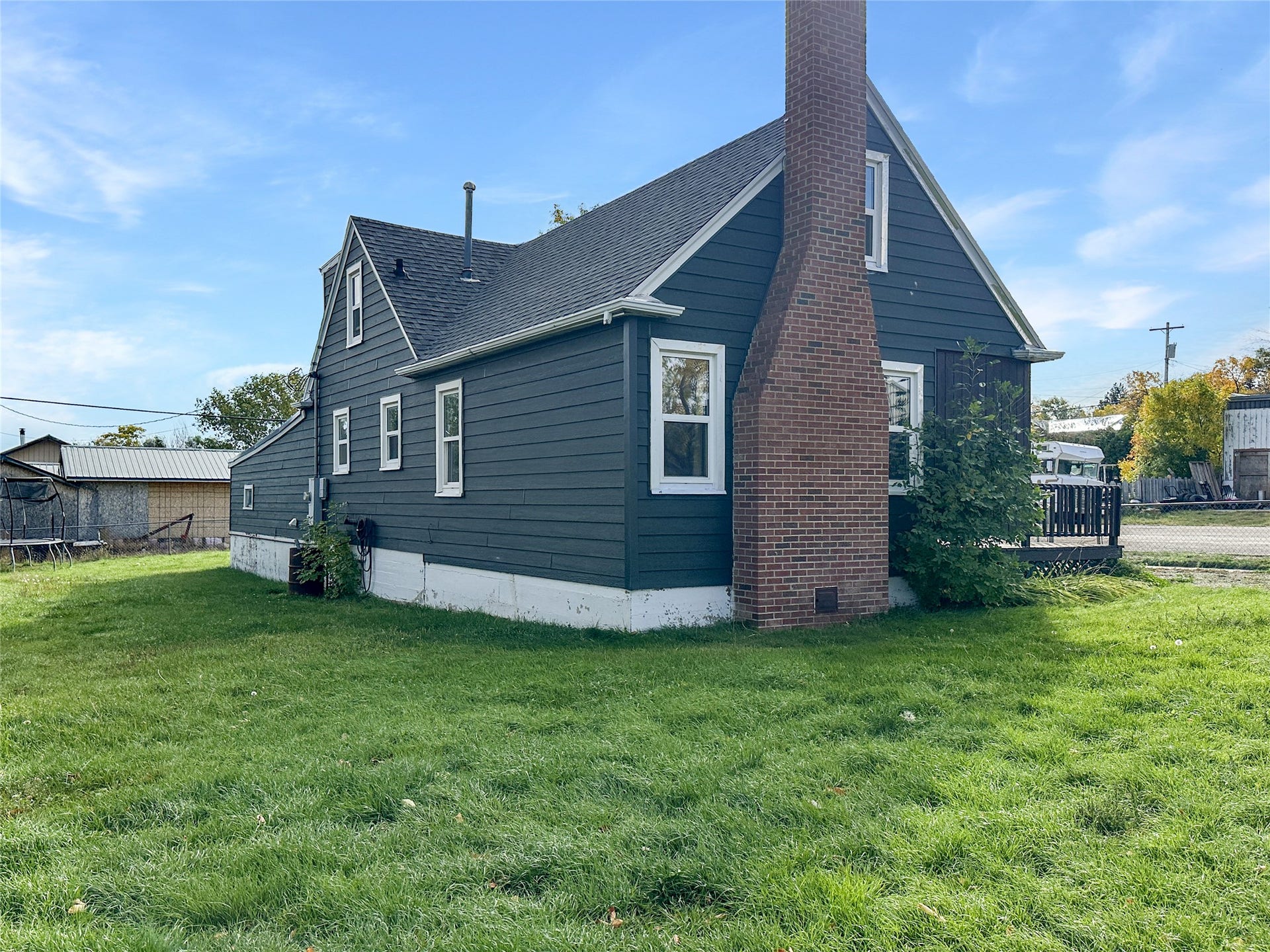 1123 2nd Street N, Shelby, MT 59474 Dark siding with white trim, a brick chimney, and a brown railing deck