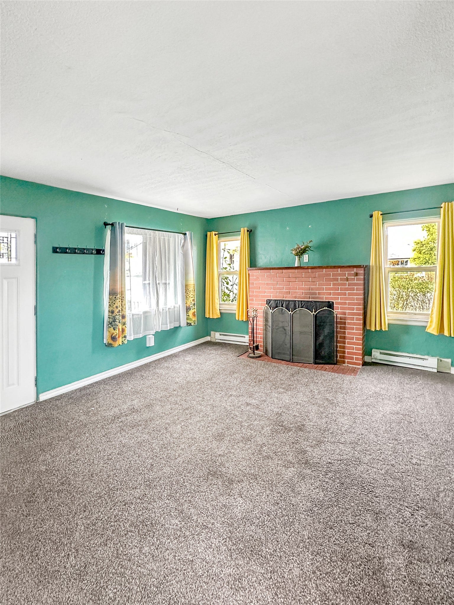 1123 2nd Street N, Shelby, MT 59474 Brick fireplace with a black metal screen, gray carpet flooring, and two windows