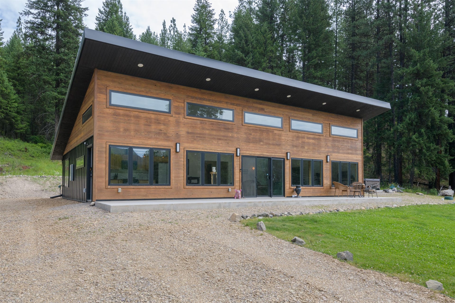 Modern architecture featuring wood-finish siding, a dark sloped roof, a gravel driveway, and a concrete patio