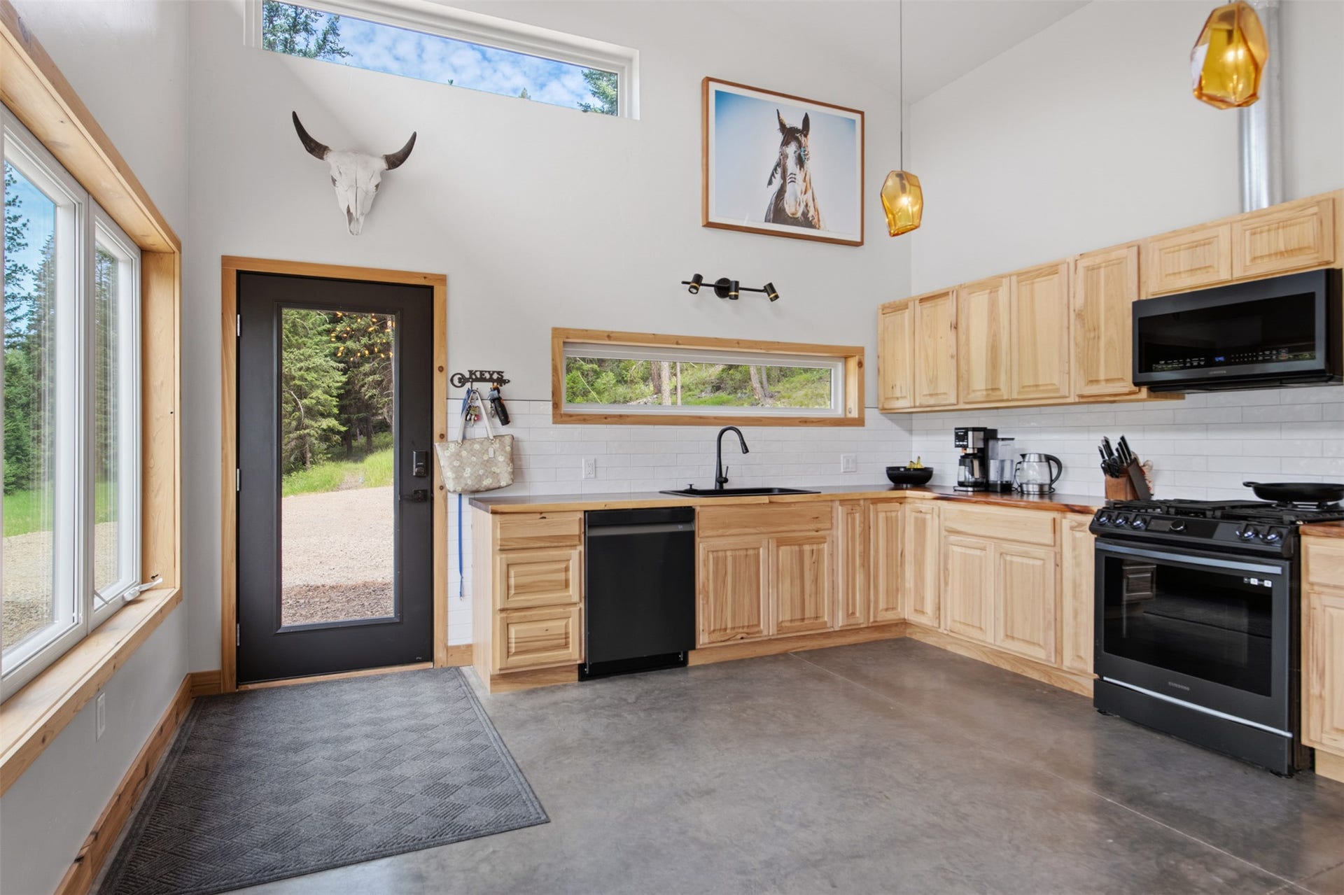 Vaulted ceiling, natural wood cabinetry, wood-finish countertops, black appliances, and a full-light entry door