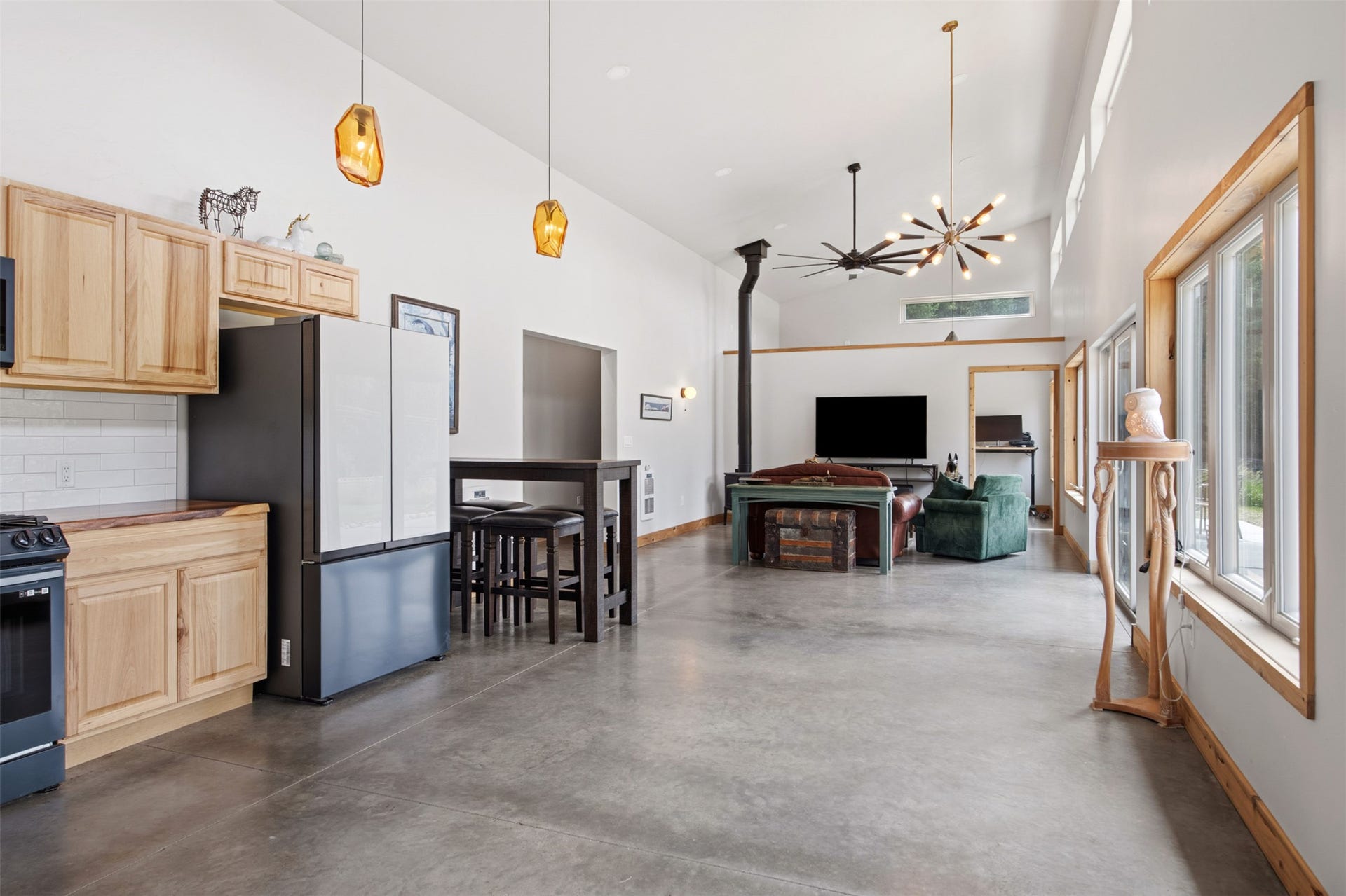 Open-concept living area featuring vaulted ceilings, wood-finish window trim, and sleek concrete flooring