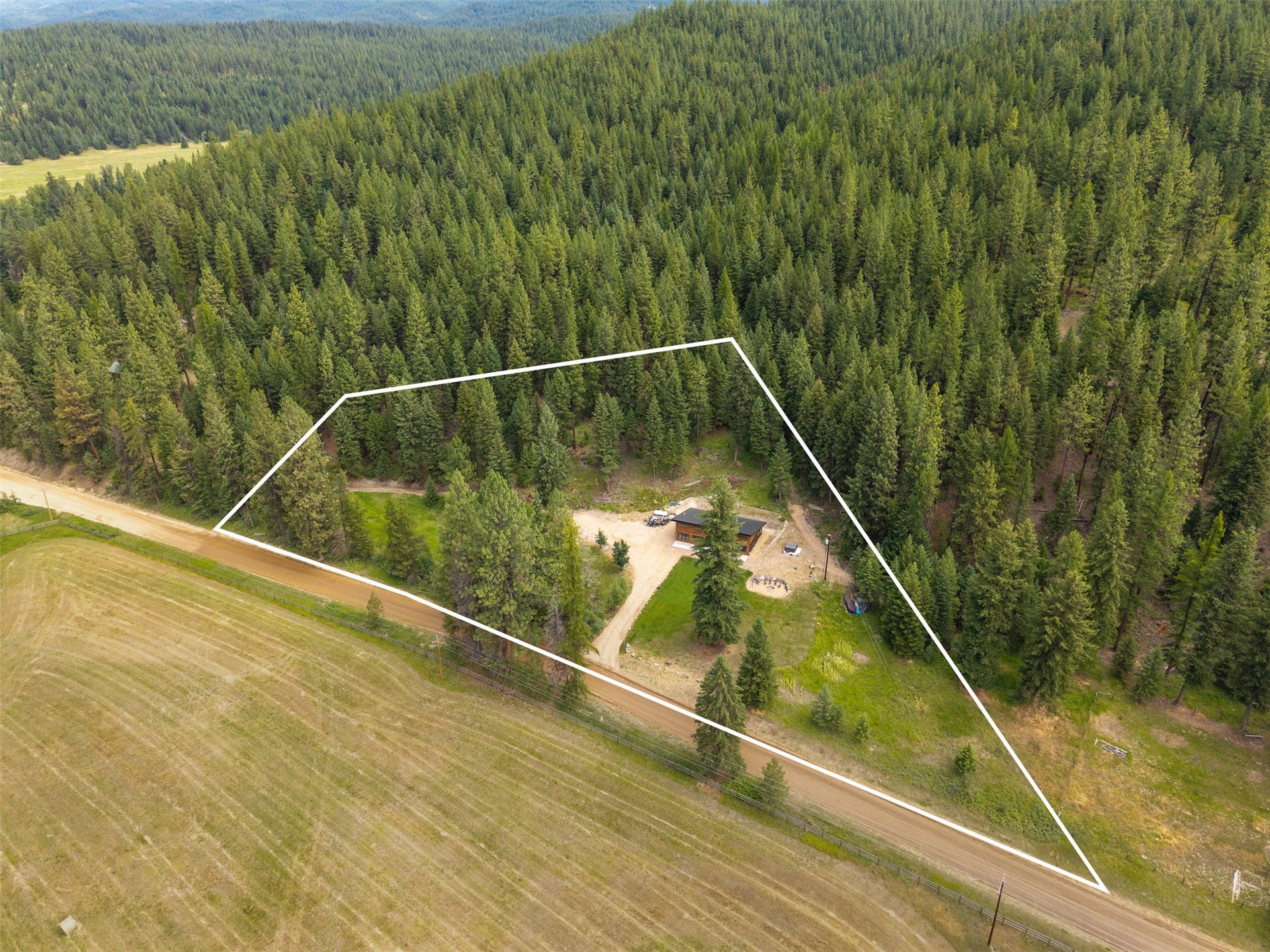Wooded acreage featuring a single-story dwelling and a gravel access road