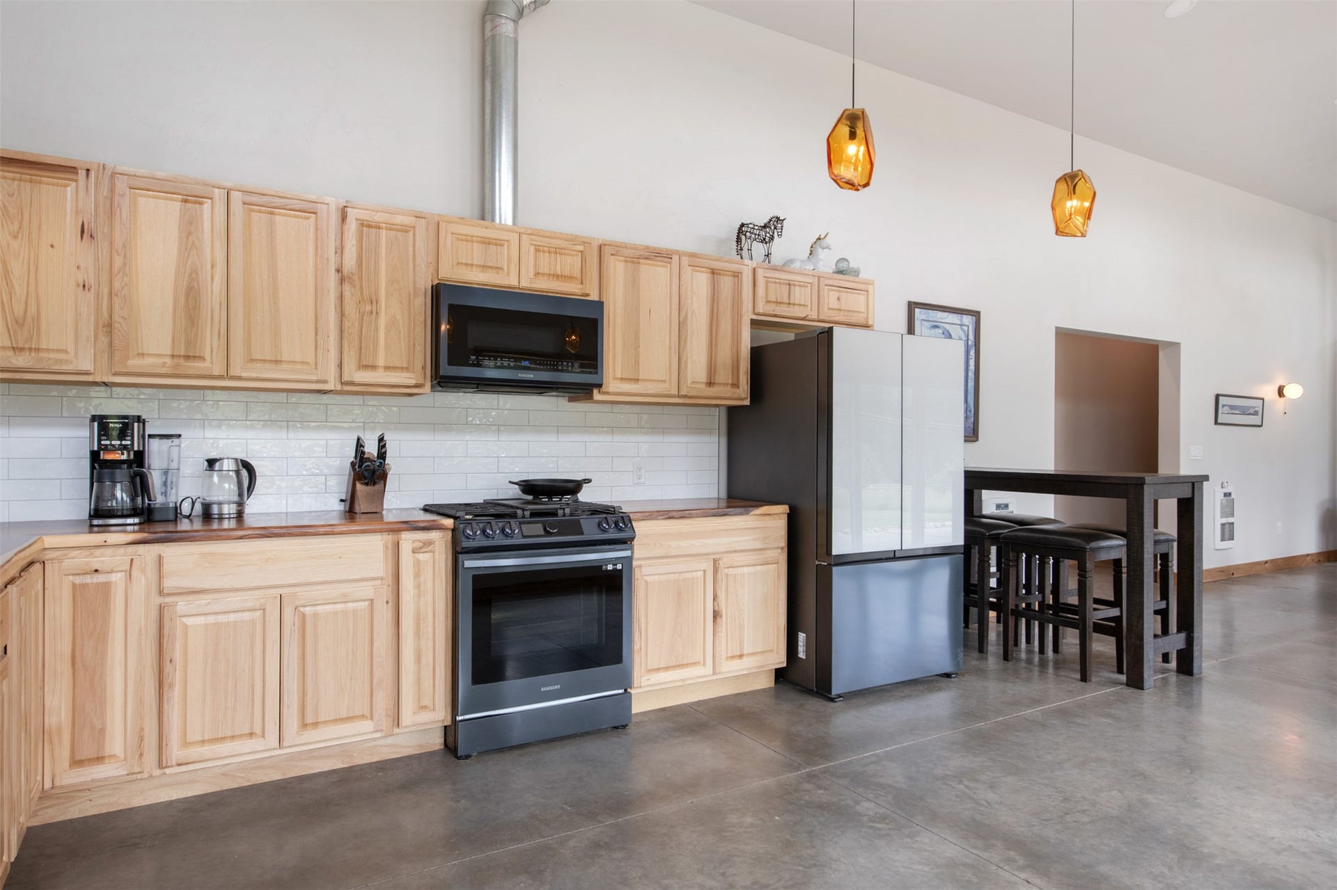 Light wood-finish cabinetry with black hardware, white subway tile backsplash, stainless steel appliances, and concrete-finish flooring