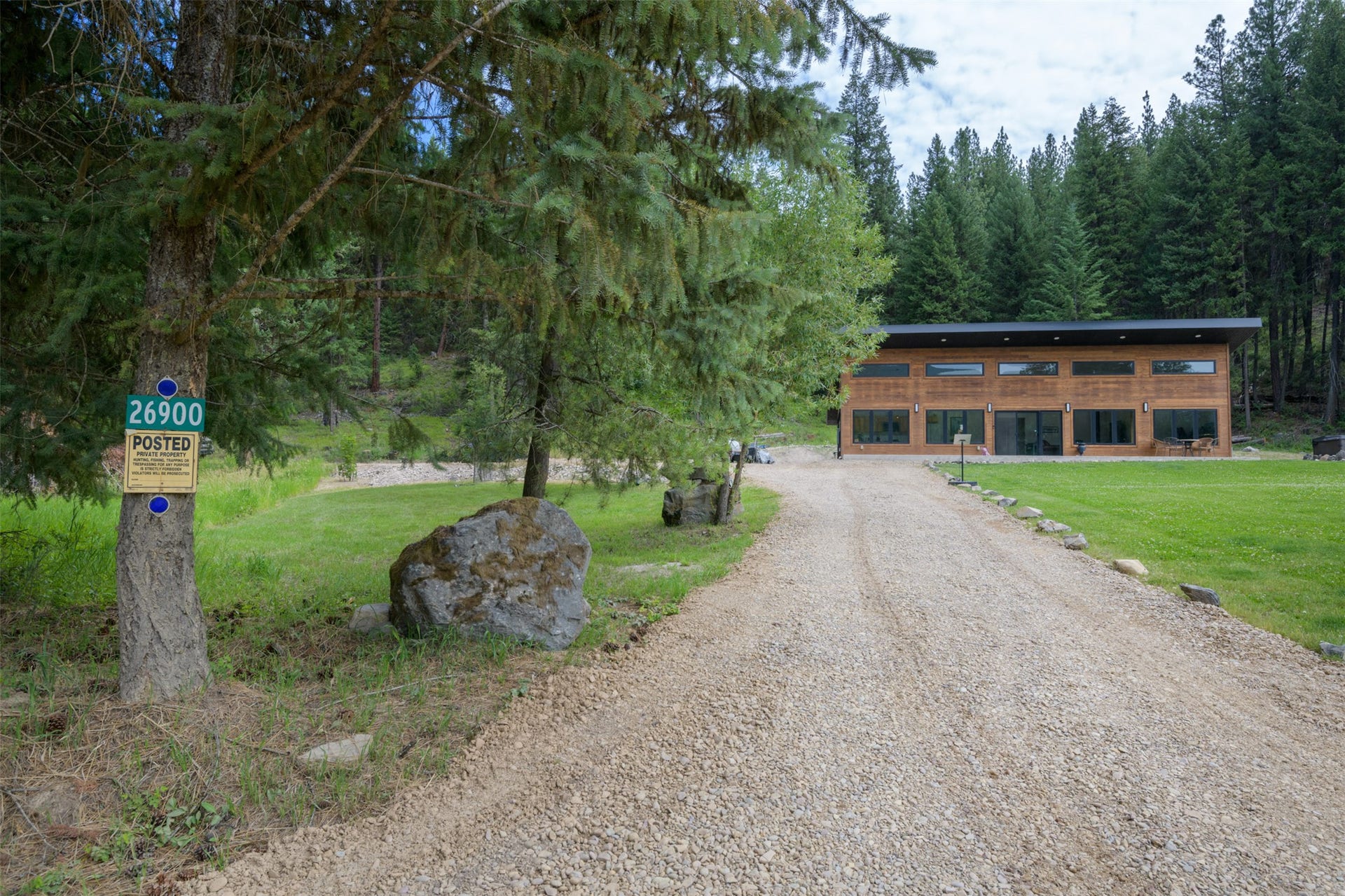 Gravel driveway leading to a contemporary residence with wood siding, expansive windows, and a flat roofline