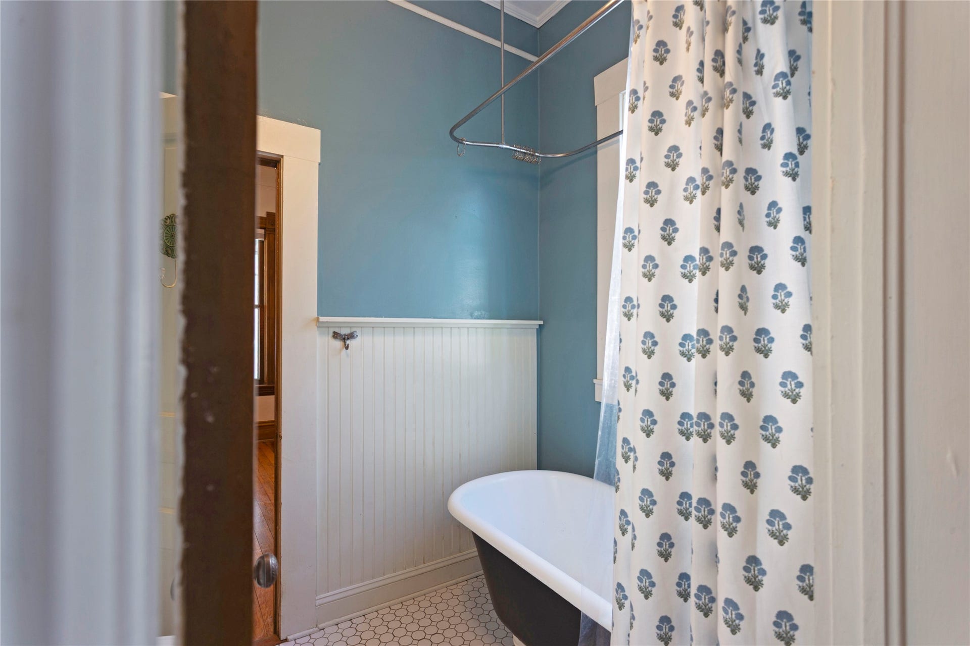 Clawfoot bathtub with an overhead shower, beadboard wainscoting, and hexagonal floor tiling