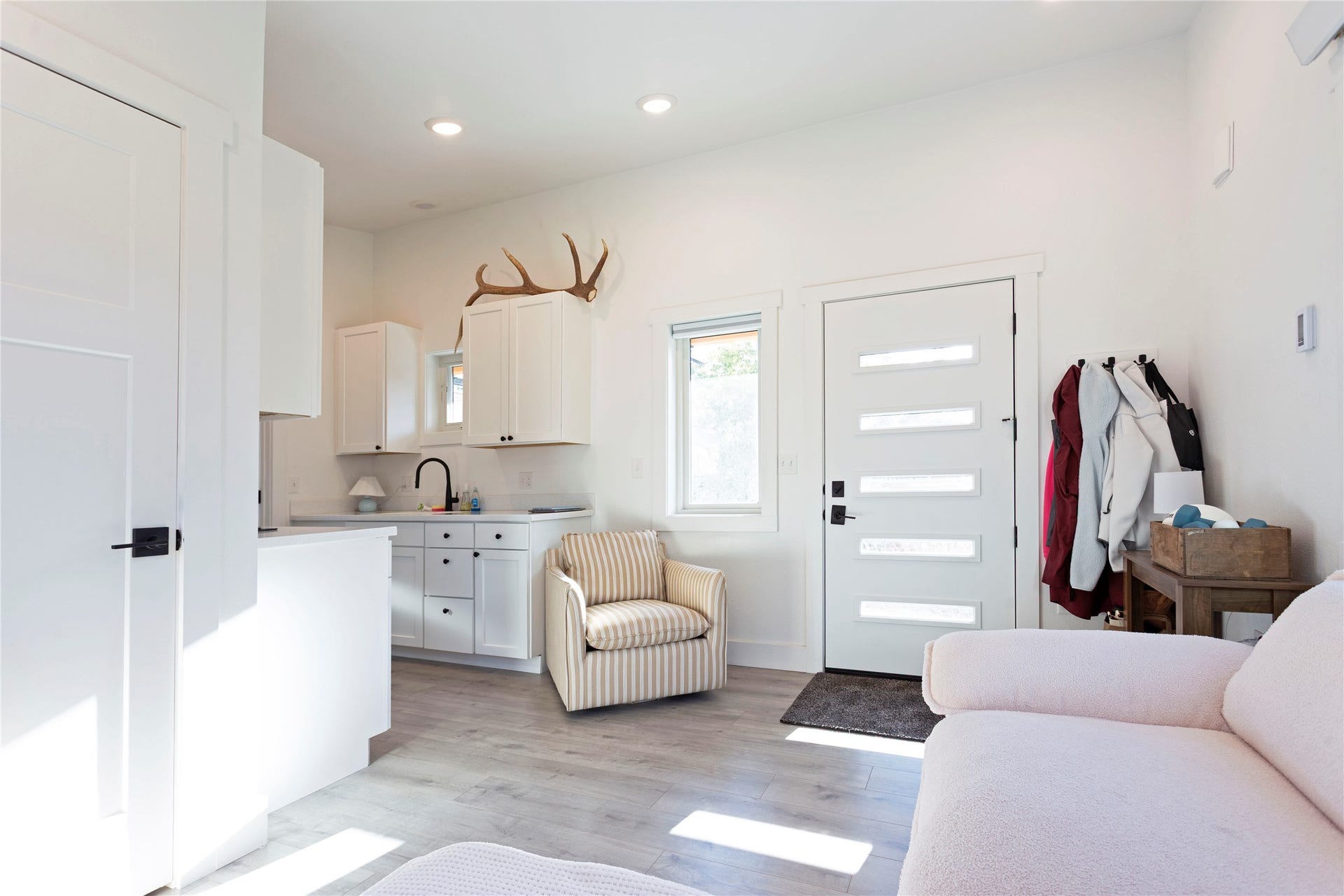 White cabinetry with black hardware, wood-finish flooring, recessed lighting, white perimeter countertops, and a modern front door with frosted glass panels