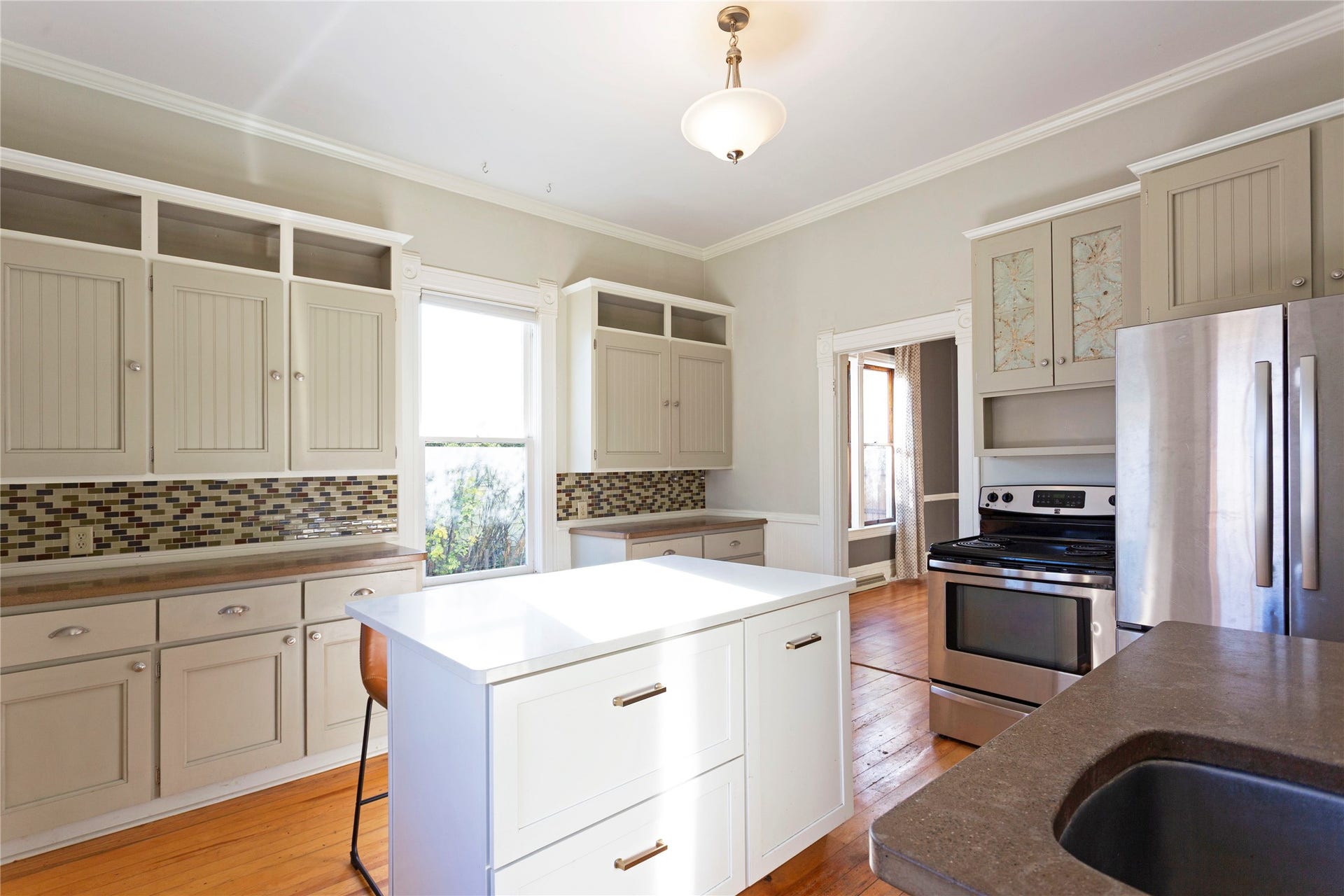 Kitchen featuring wood-finish flooring, a white center island, a stainless steel refrigerator, a stainless steel range, and mosaic tile backsplash