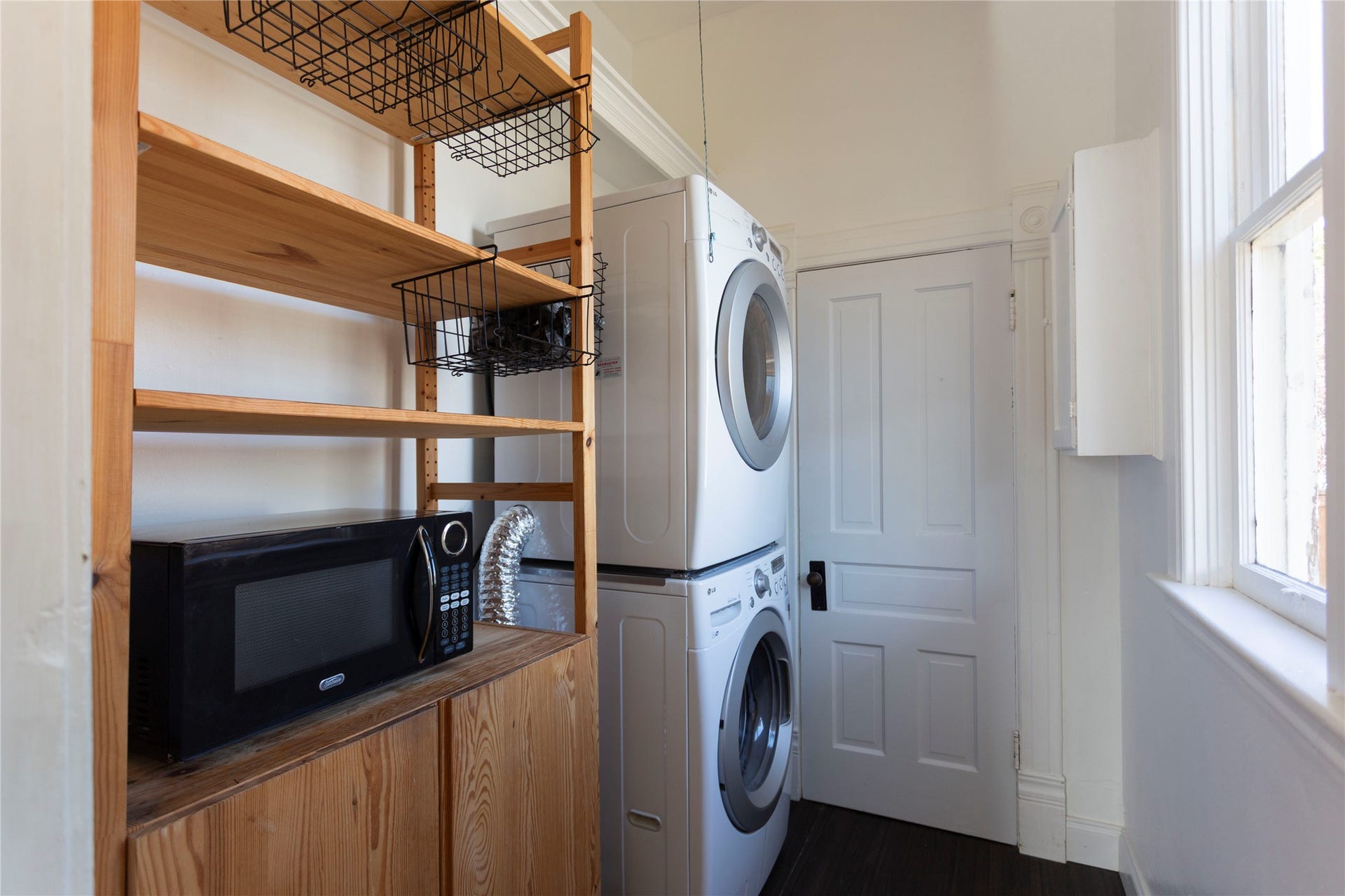 Stacked washer and dryer units, wood-finish shelving, and a paneled door
