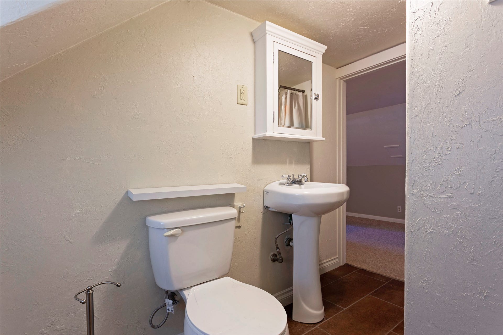 Pedestal sink with chrome fixtures, white medicine cabinet, and tiled flooring