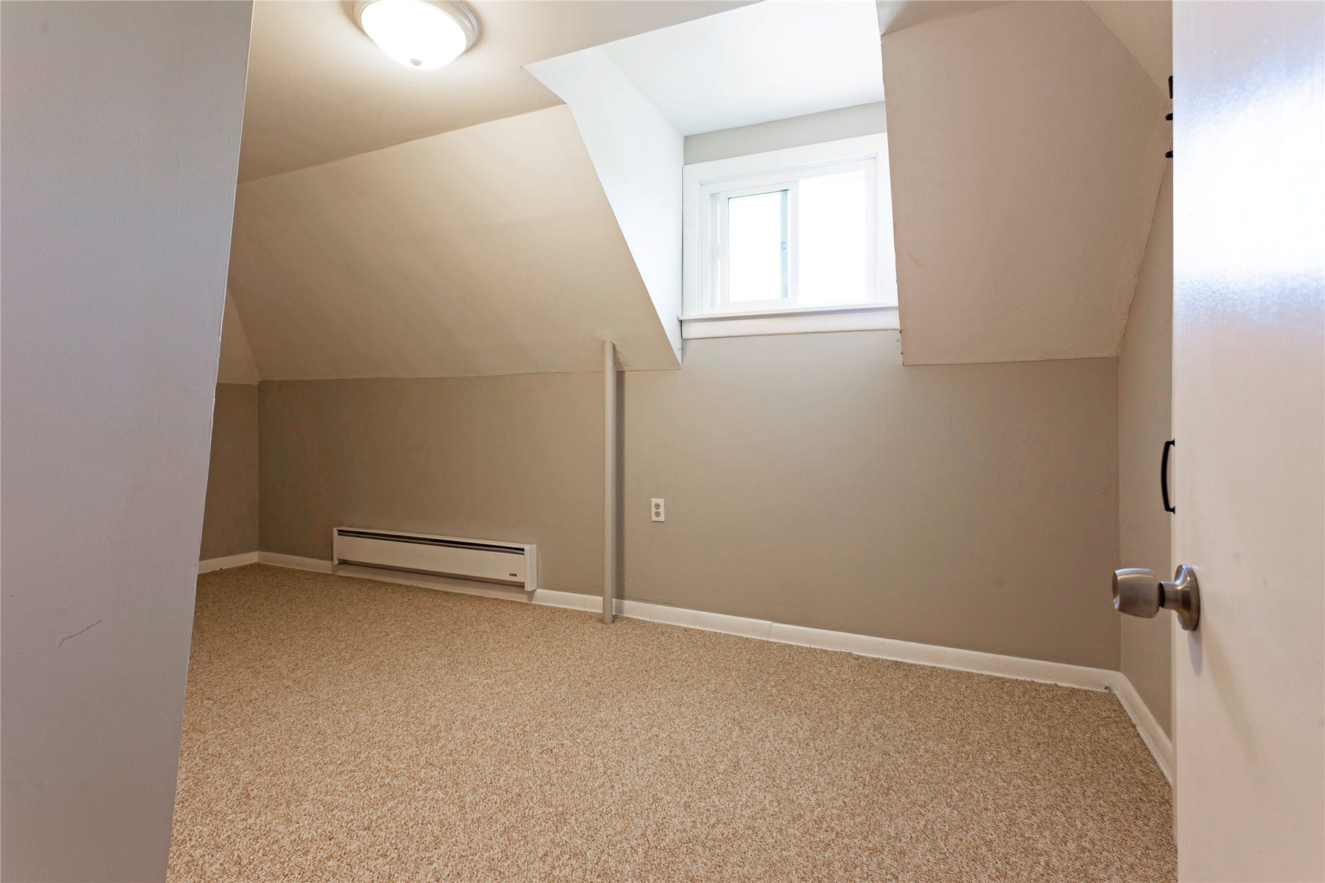 Sloping ceiling room featuring a window, wall-mounted heating unit, flush mount ceiling light, and carpeted flooring