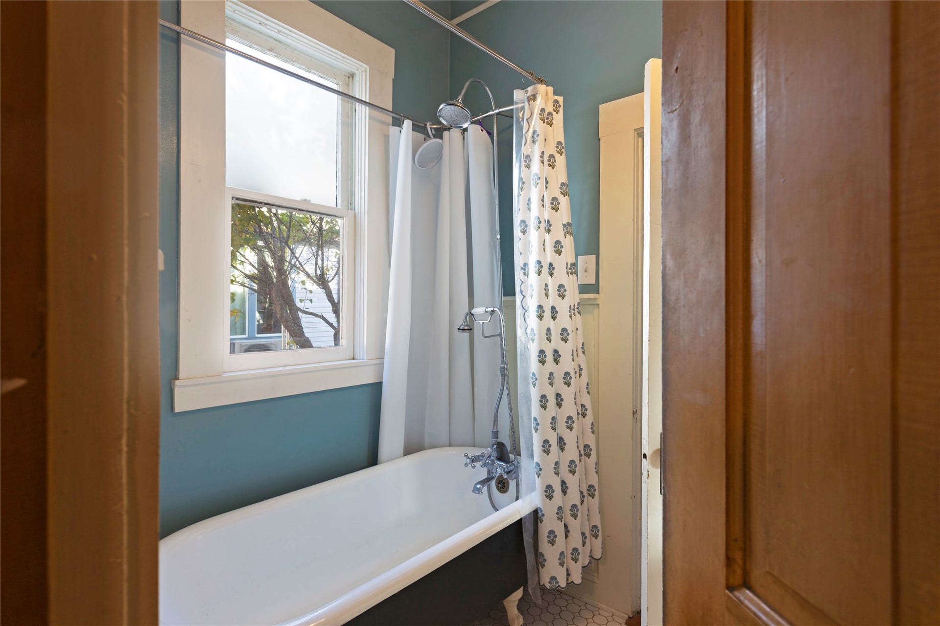 Clawfoot tub with a shower attachment, complemented by a single-hung window with privacy glass, and hexagonal tile flooring