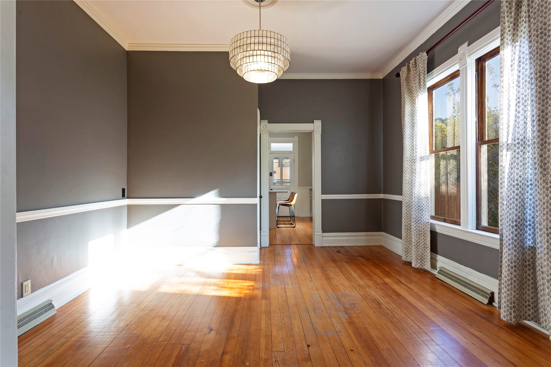 Hardwood flooring with a polished finish, crown molding, double-hung windows, and a decorative ceiling light fixture