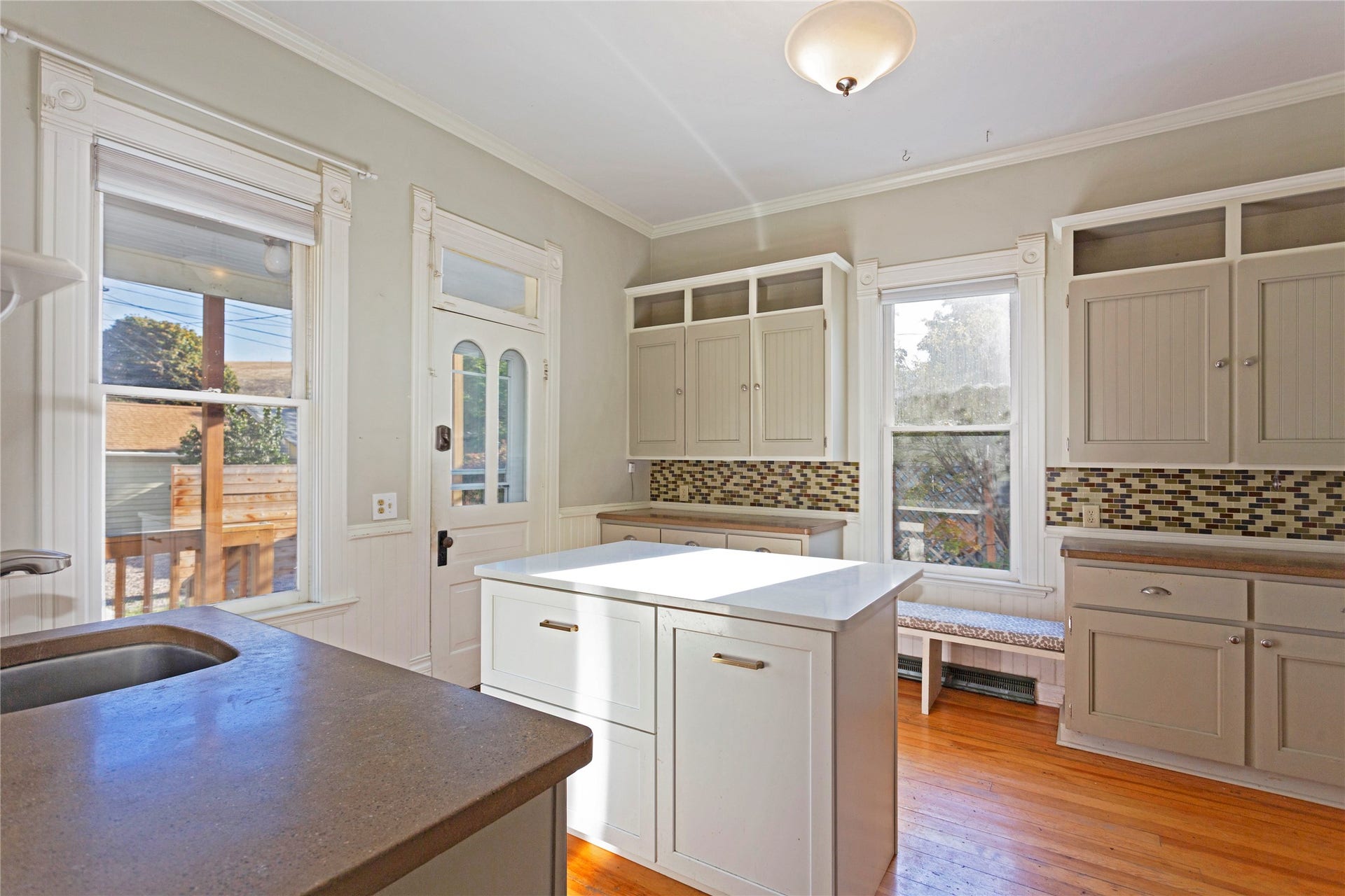 Kitchen featuring a central island with a white countertop, wood-finish flooring, white paneled cabinets, a mosaic tile backsplash, and a built-in window bench