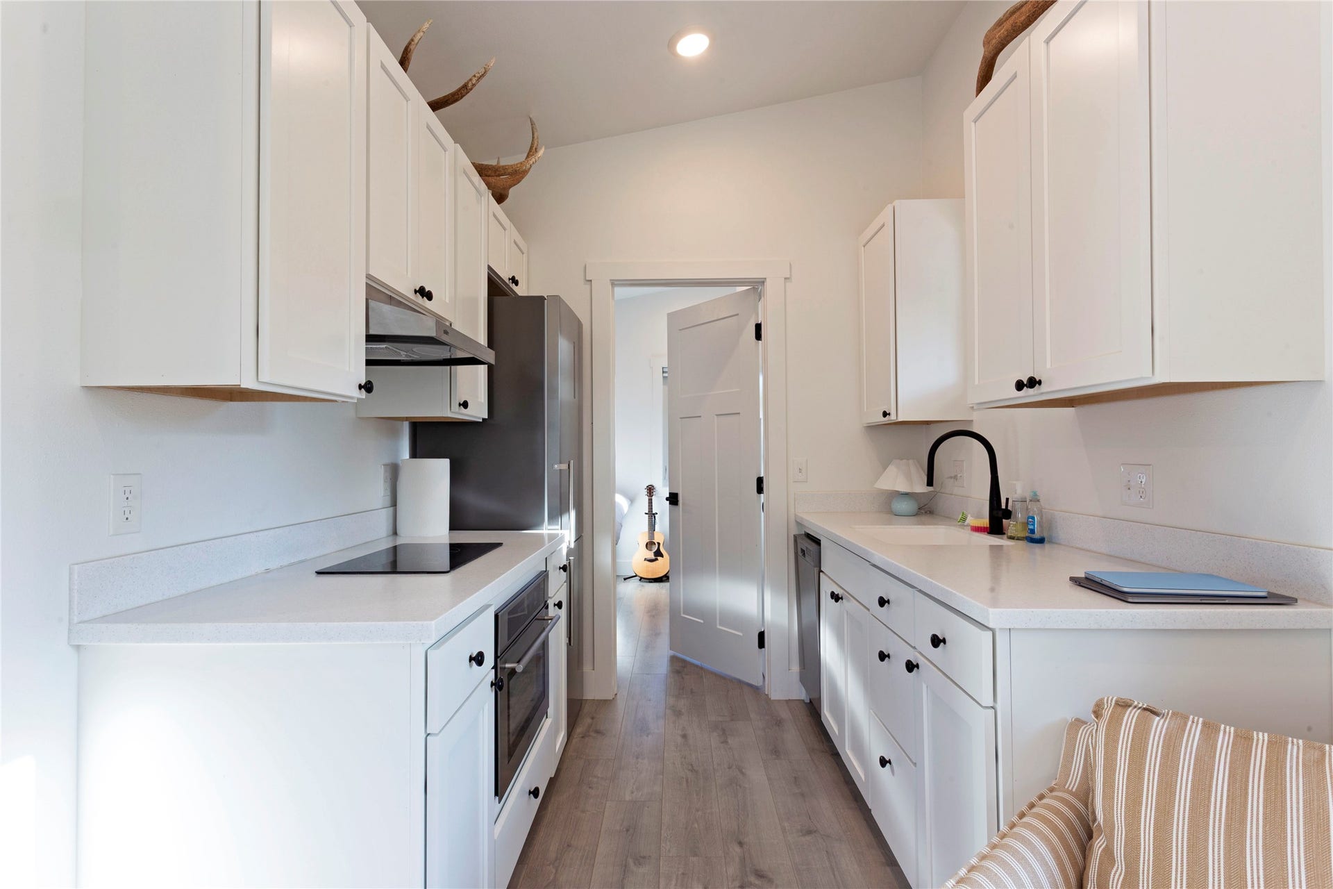 Galley-style kitchen featuring white cabinetry, light-toned countertops, a built-in cooktop, a wall oven, and wood-finish flooring
