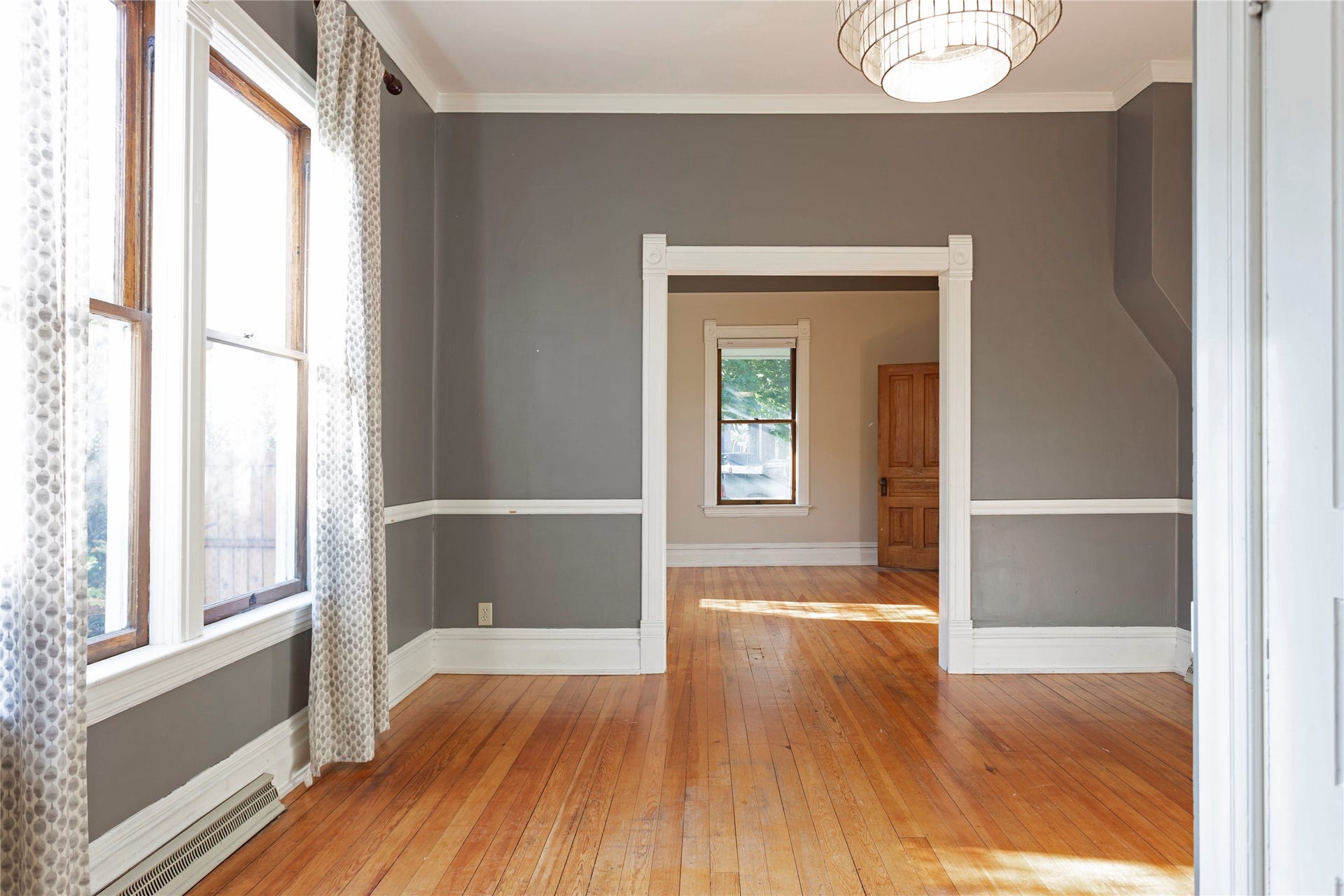Hardwood flooring, painted wainscoting, crown molding, and a decorative ceiling light fixture