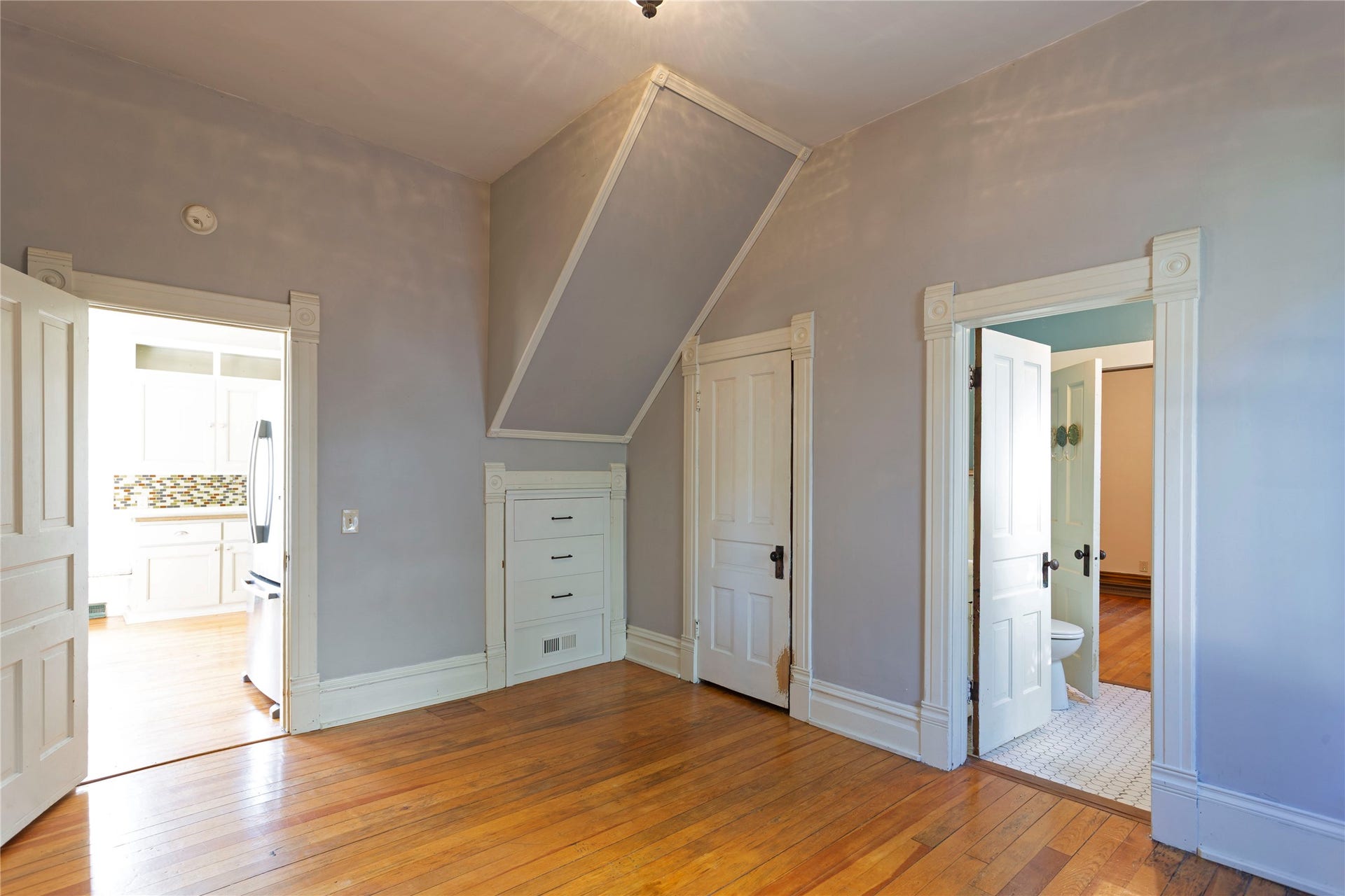 Hardwood flooring, white trim details, built-in cabinetry, white doors, and a sloped ceiling