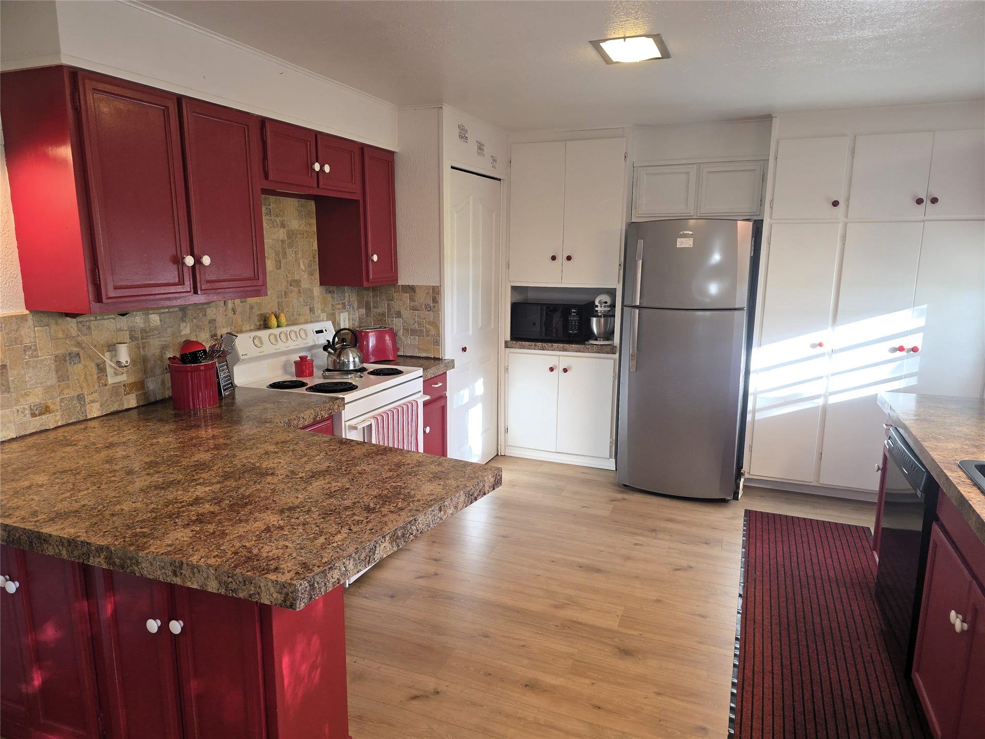 115 Ricketts Road, Hamilton, MT 59840 Kitchen featuring wood-finish flooring, red and white cabinetry, brown speckled countertops, and a tiled backsplash