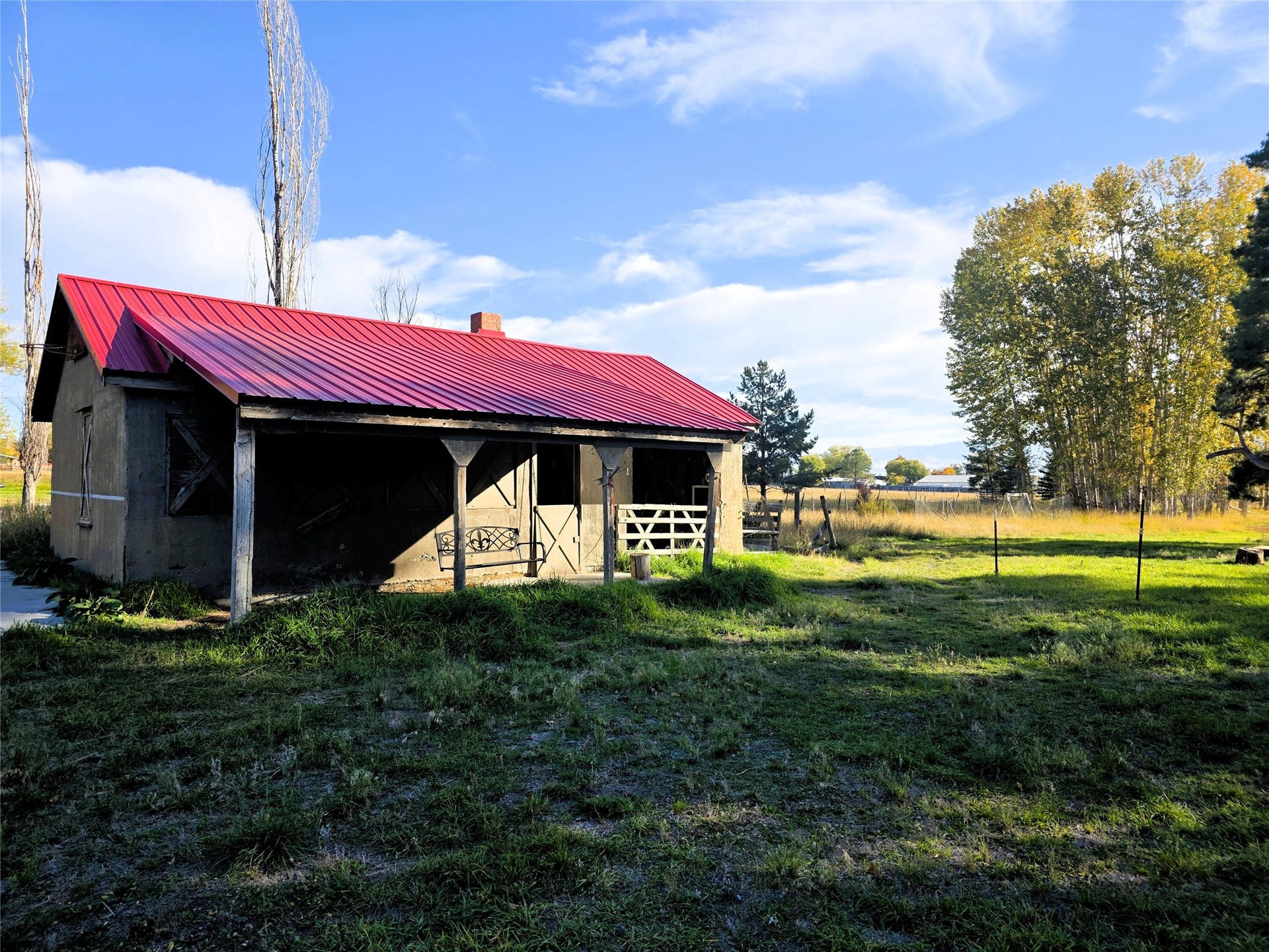 115 Ricketts Road, Hamilton, MT 59840 Structure featuring a red corrugated metal roof, covered porch with wooden support posts, and a field with mature trees