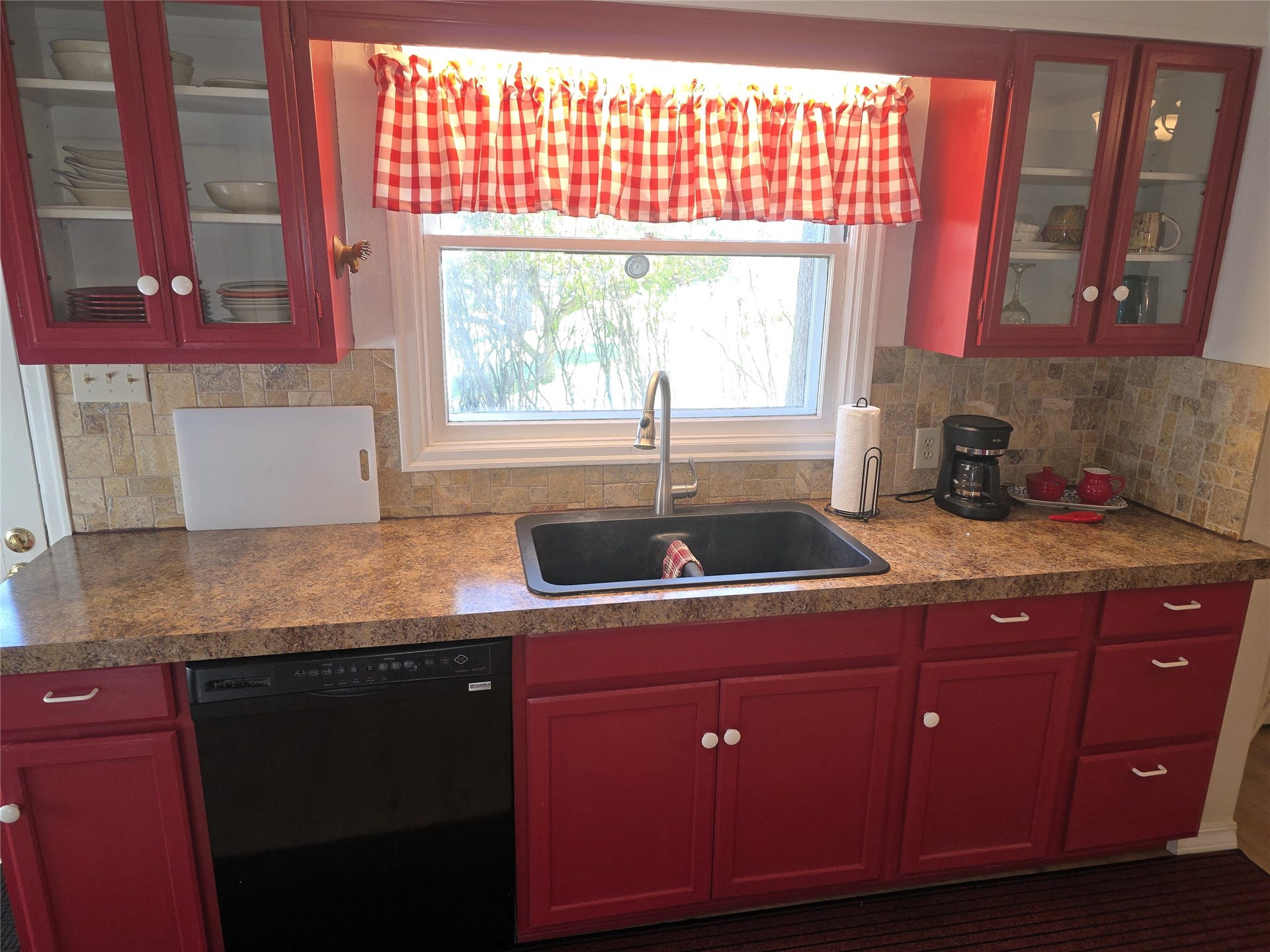 115 Ricketts Road, Hamilton, MT 59840 Red cabinetry with white knobs, a dark sink basin with a gooseneck faucet, light-toned countertop, and a mosaic tile backsplash