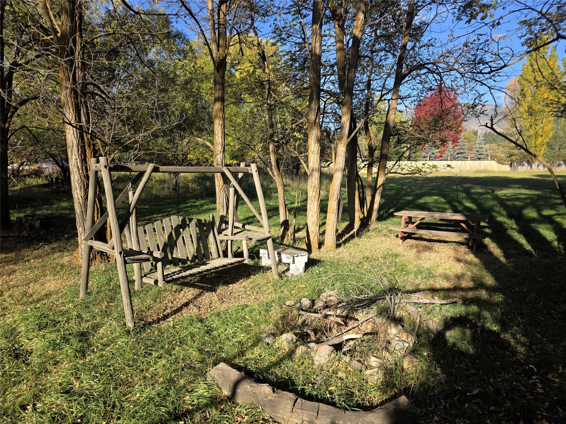115 Ricketts Road, Hamilton, MT 59840 Expansive natural yard featuring mature trees, a wooden swing, a picnic table, and a defined fire pit area