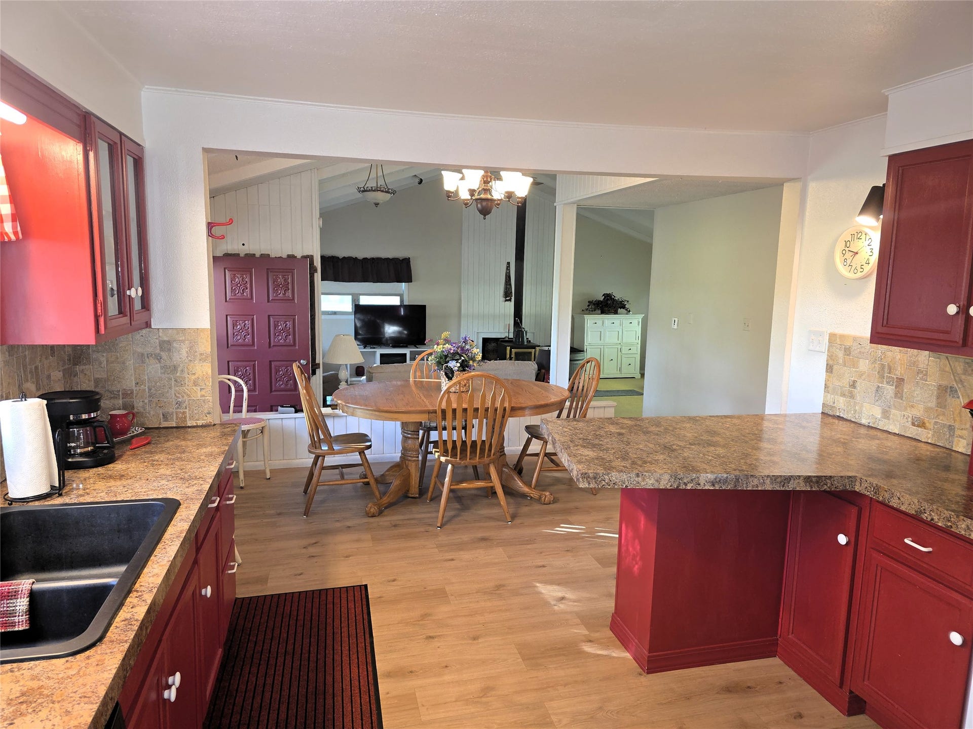 115 Ricketts Road, Hamilton, MT 59840 Red cabinetry with white knobs, wood-finish flooring, a stone-look backsplash, and a breakfast bar