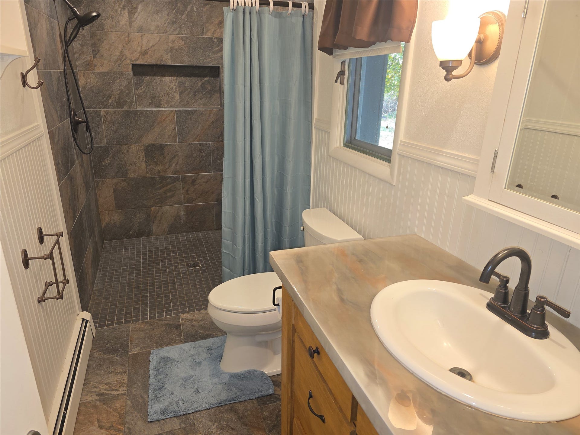 115 Ricketts Road, Hamilton, MT 59840 Tiled shower with built-in niche, wood-finish vanity with countertop, wall-mounted light fixture, and beadboard paneling