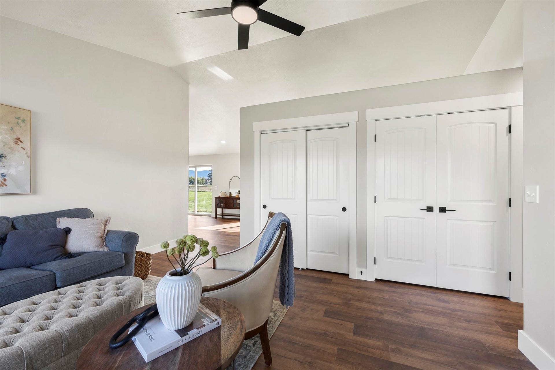 Vaulted ceiling, wood-finish flooring, white panel doors, matte black door hardware, and a ceiling fan with integrated lighting