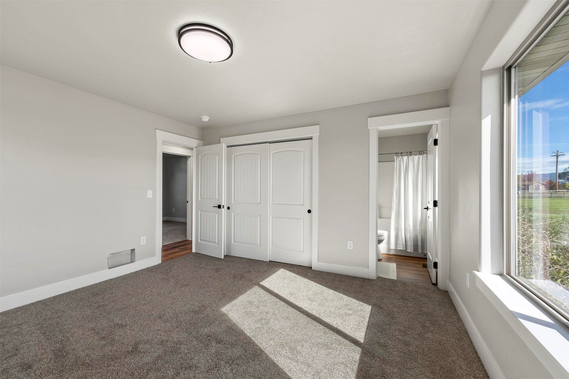 Plush carpet flooring, a large window, white trim and interior doors, and a ceiling-mounted light fixture