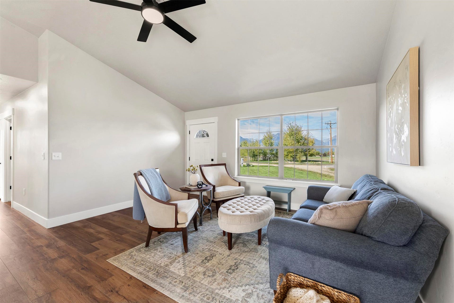 Vaulted ceilings, wood-finish flooring, white trim, and a window with exterior scenery