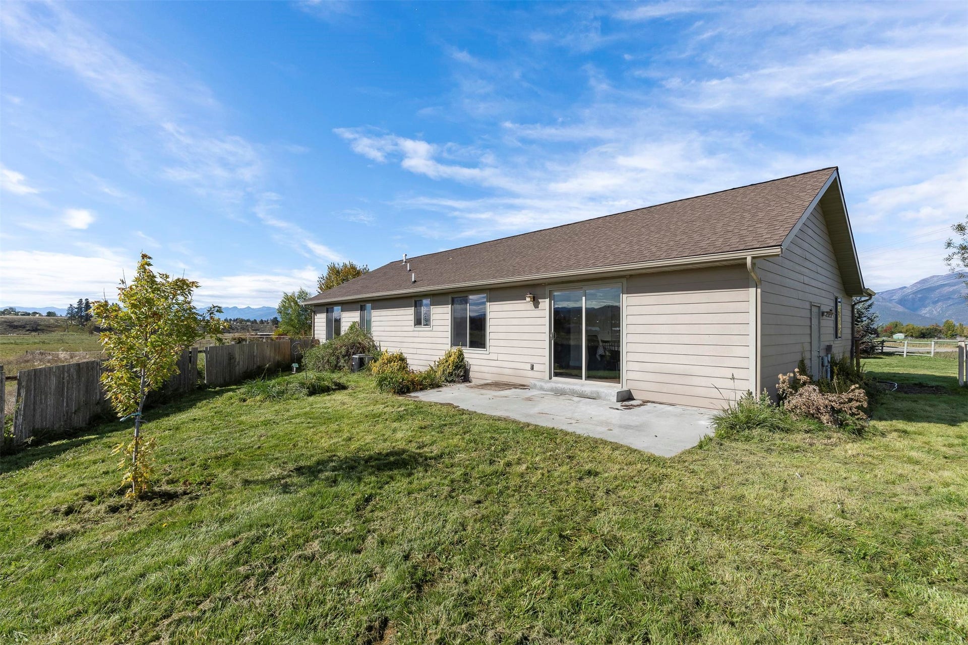 Sliding glass door access to an outdoor patio with a mountain backdrop, complemented by a wooden fence and a grassy yard
