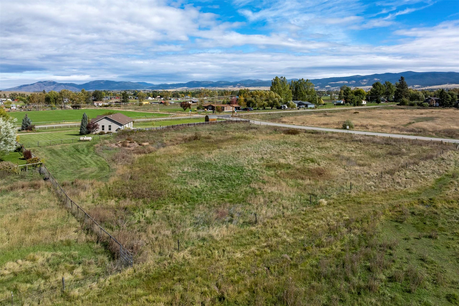 Expansive land parcel featuring open fields, a partial perimeter fence, and distant mountain backdrops