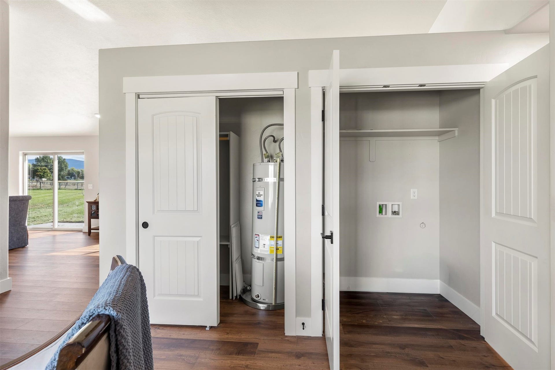 Utility closet with a hot water heater and an additional closet with laundry hookups, featuring wood-finish flooring and white trim