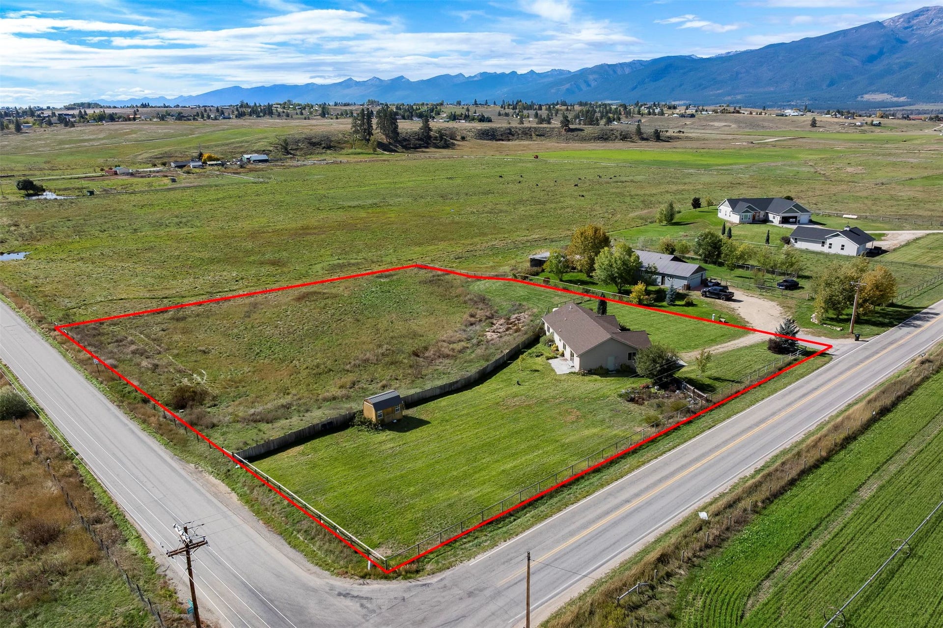 Expansive lot featuring a single-story residence with a brown roof, a well-maintained lawn, and a gravel driveway